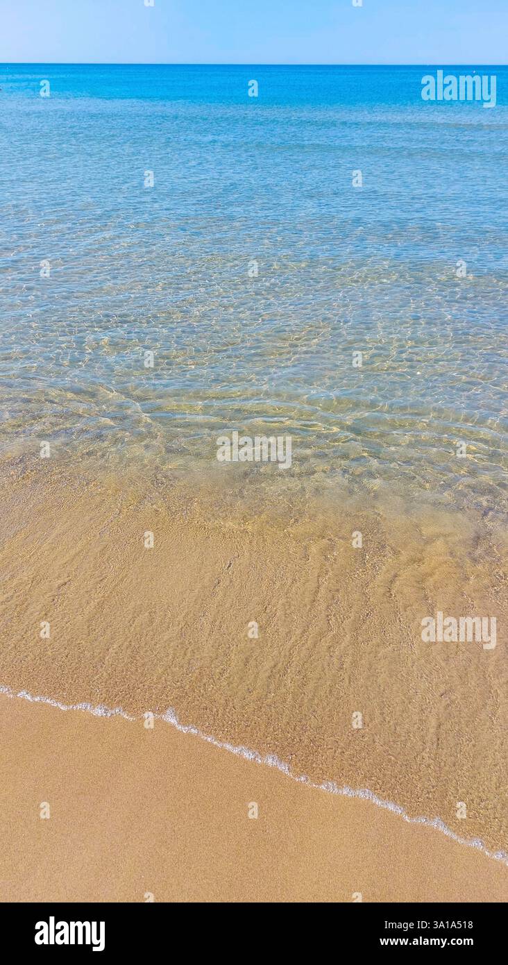 Ruhige Szene mit kristallklarem Wasser, das sanft am goldenen Sandstrand an sonnigen Tagen plätschert Stockfoto