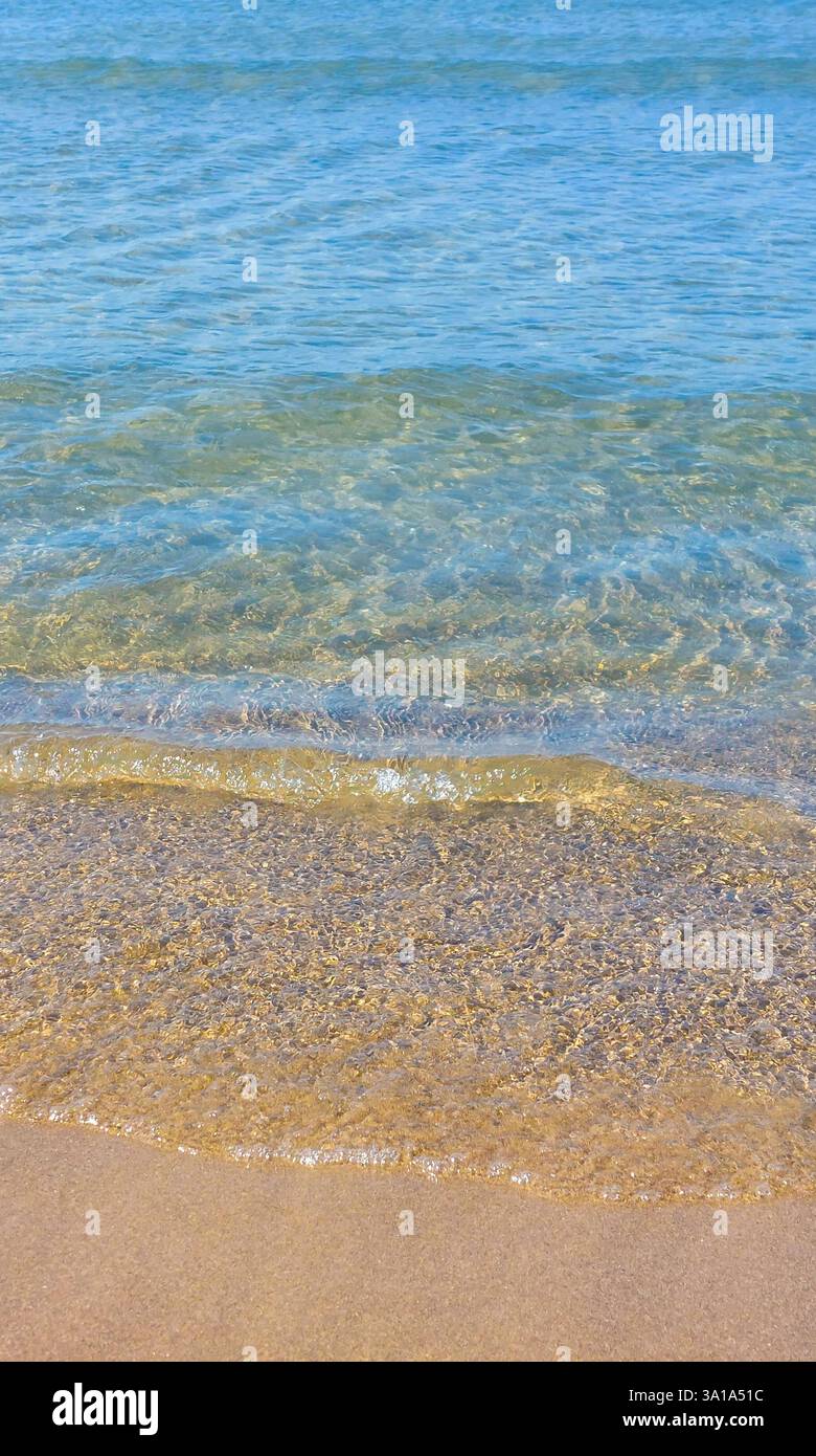 Ruhige Szene mit kristallklarem Wasser, das sanft auf einem goldenen Sandstrand plätschert und eine ruhige und einladende Atmosphäre schafft Stockfoto