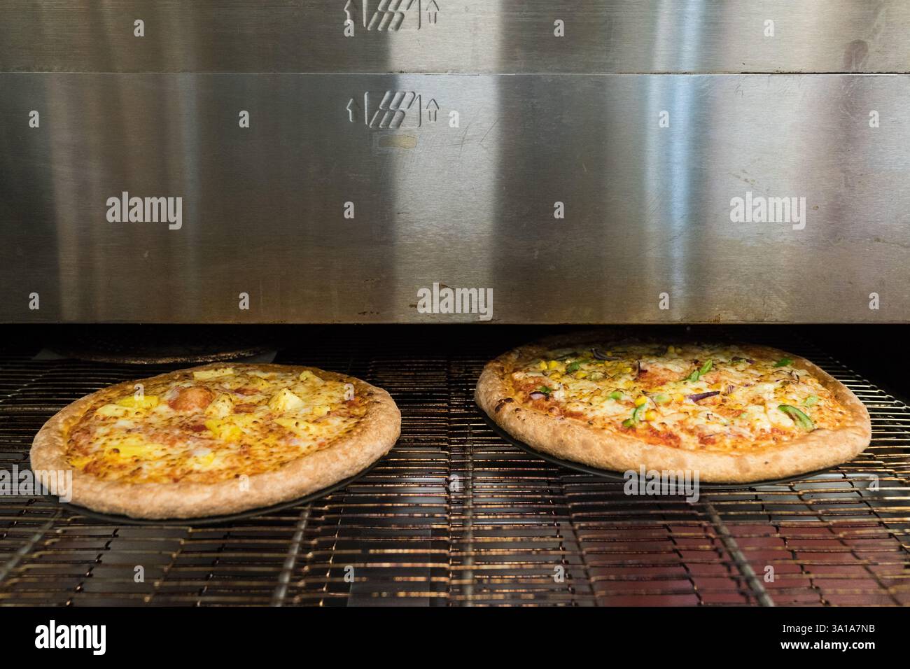 Pizza (hawaiianisch & vegetarisch) wird in einem kommerziellen Pizzaofen gekocht. Stockfoto