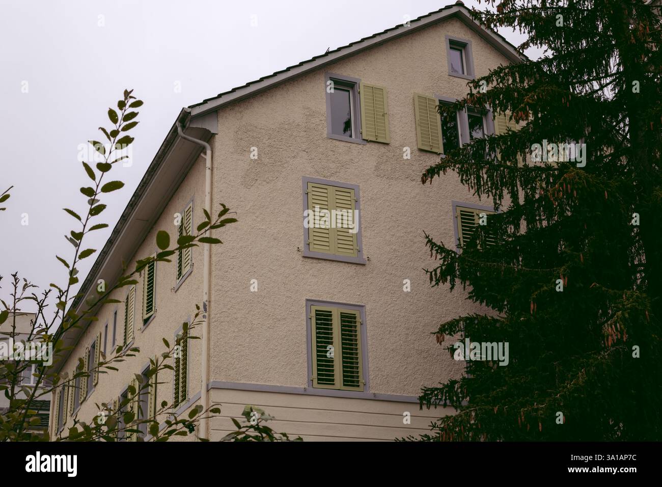 Ein klassisches Wohngebäude mit hellen Stuckwänden und leuchtenden grünen Fensterläden, das eine ruhige und einladende Atmosphäre bietet. Die Gebäude-fea Stockfoto