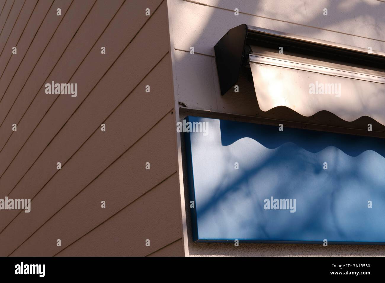 Nahaufnahme einer Markise an der Wand eines Ladens. Die Sonne ist niedrig und wirft harte Schatten von den Bäumen gegenüber an der Hauswand. Stockfoto