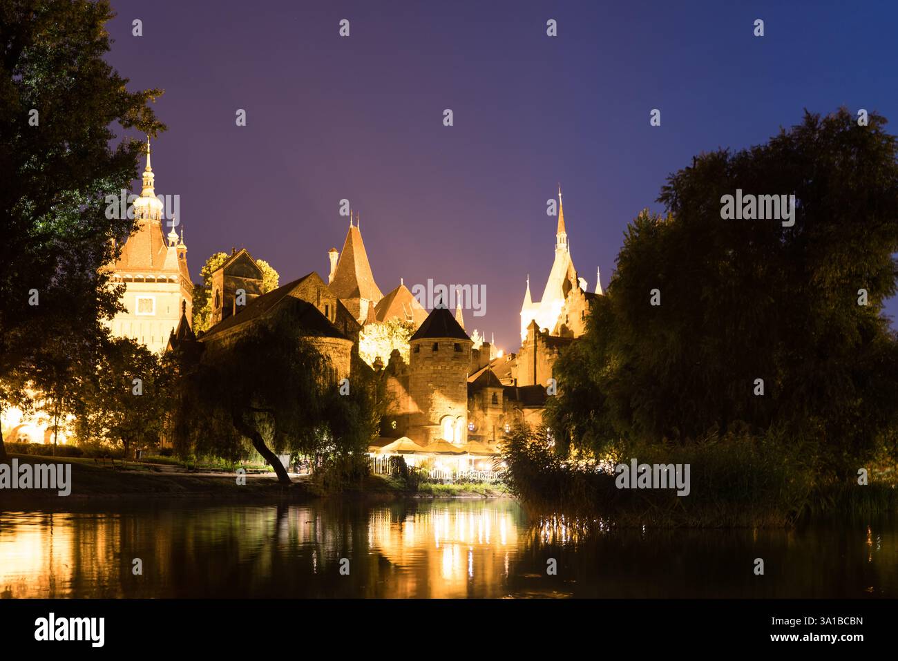 Nächtlicher Blick auf das Schloss Vajdahunyad in Budapest, Ungarn, das sich auf dem nahe gelegenen Fluss spiegelt. Bei Nacht beleuchtet. Stockfoto