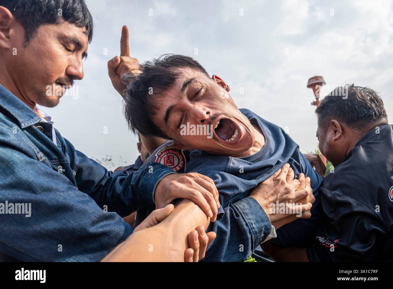 Bang Phra, Nakhon Pathom, Thailand. März 2025. Ein Gläubiger, der Sak Yant Tattoos trägt, Gerät in einen Zustand gewalttätiger Geisterbesessenheit und wird von den Teilnehmern während der jährlichen Wai Kru Zeremonie im Wat Bang Phra in Nakhon Pathom, Thailand, zurückgehalten. Der Tempel Wat Bang Phra, 40 km von der thailändischen Hauptstadt Bangkok entfernt, findet einmal im Jahr die Wai Gru Zeremonie statt. Der Name des Tempels wird übersetzt mit Kloster des Flussufers Buddha Bild. Sak Yant Tattoos sind hochstilisierte Tattoos buddhistischer Gebete und religiöser Symbole, die den Gläubigen, die sie einsetzen lassen, besonderen Schutz und andere Vorteile bieten Stockfoto