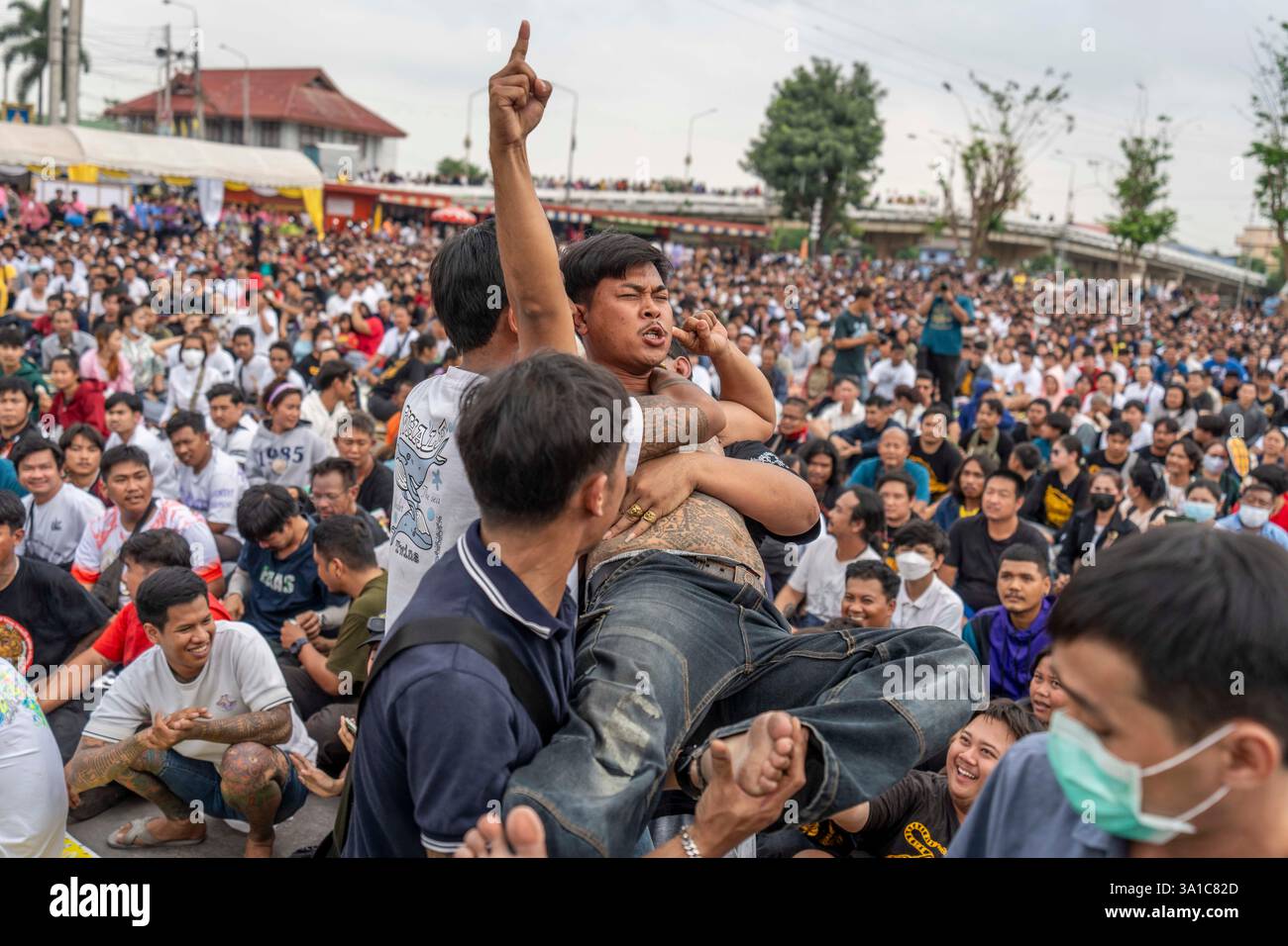Bang Phra, Nakhon Pathom, Thailand. März 2025. Ein Gläubiger, der Sak Yant Tattoos trägt, Gerät in einen Zustand gewalttätiger Geisterbesessenheit und wird von den Teilnehmern während der jährlichen Wai Kru Zeremonie im Wat Bang Phra in Nakhon Pathom, Thailand, zurückgehalten. Der Tempel Wat Bang Phra, 40 km von der thailändischen Hauptstadt Bangkok entfernt, findet einmal im Jahr die Wai Gru Zeremonie statt. Der Name des Tempels wird übersetzt mit Kloster des Flussufers Buddha Bild. Sak Yant Tattoos sind hochstilisierte Tattoos buddhistischer Gebete und religiöser Symbole, die den Gläubigen, die sie einsetzen lassen, besonderen Schutz und andere Vorteile bieten Stockfoto