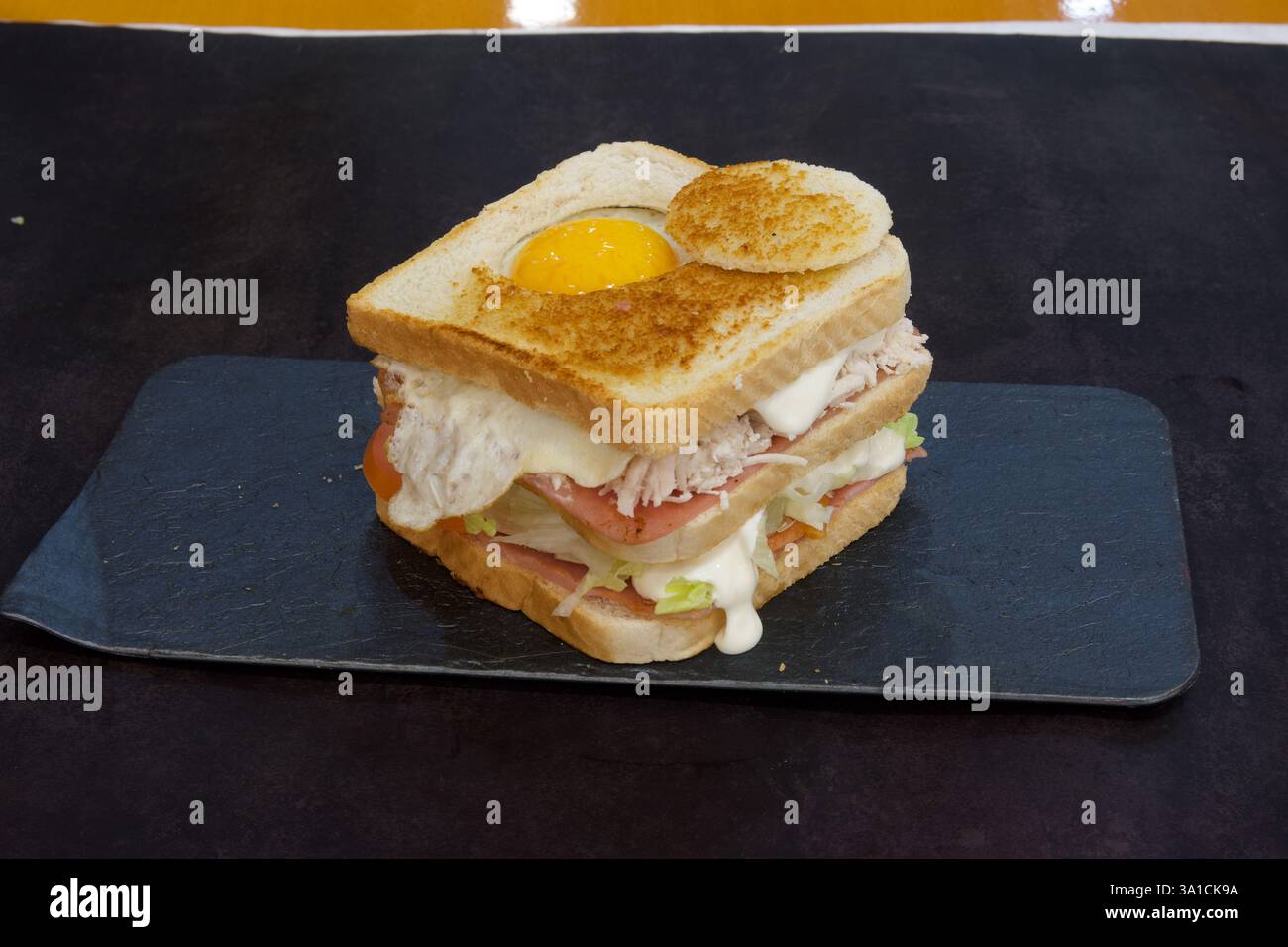 Ein Sandwich mit einem Spiegelei drauf. Das Sandwich besteht aus zwei Brotstücken mit einer Schicht Schinken und Salat dazwischen Stockfoto