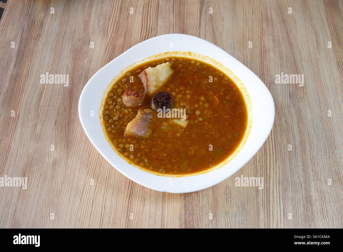Eine Schüssel Suppe mit Fleisch und Bohnen darin. Die Schüssel ist weiß und die Suppe orange Stockfoto