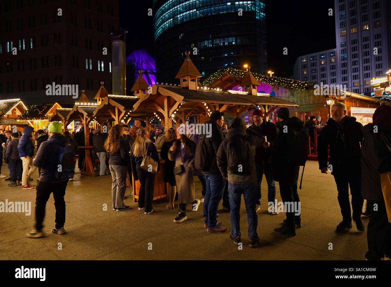 Eine große Gruppe von Menschen versammelt sich auf dem Weihnachtsmarkt am Potsdamer Platz, um an diesem Winterabend warme Speisen und Glühwein zu genießen Stockfoto