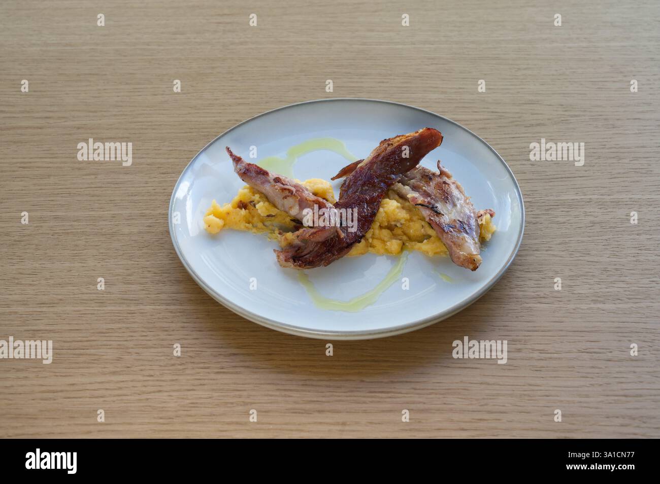 Ein Teller mit Speck und Eiern mit einem Spritzer Olivenöl. Der Speck ist gekocht und die Eier sind gerührt. Der Teller steht auf einem Holztisch Stockfoto