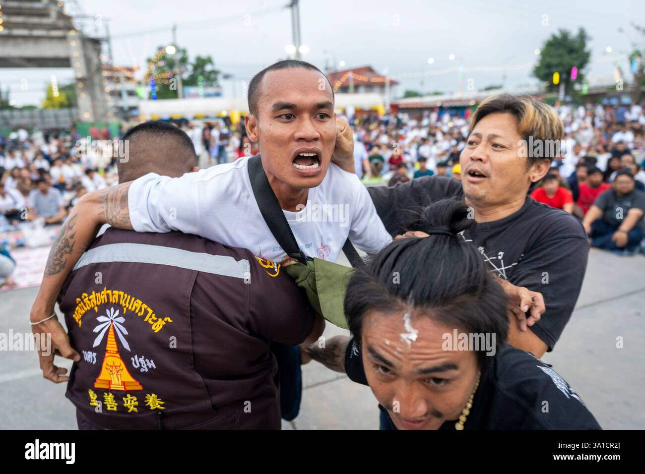 Bang Phra, Nakhon Pathom, Thailand. März 2025. Ein Gläubiger, der Sak Yant Tattoos trägt, Gerät in einen Zustand gewalttätiger Geisterbesessenheit und wird von den Teilnehmern während der jährlichen Wai Kru Zeremonie im Wat Bang Phra in Nakhon Pathom, Thailand, zurückgehalten. Der Tempel Wat Bang Phra, 40 km von der thailändischen Hauptstadt Bangkok entfernt, findet einmal im Jahr die Wai Gru Zeremonie statt. Der Name des Tempels wird übersetzt mit Kloster des Flussufers Buddha Bild. Sak Yant Tattoos sind hochstilisierte Tattoos buddhistischer Gebete und religiöser Symbole, die den Gläubigen, die sie einsetzen lassen, besonderen Schutz und andere Vorteile bieten Stockfoto