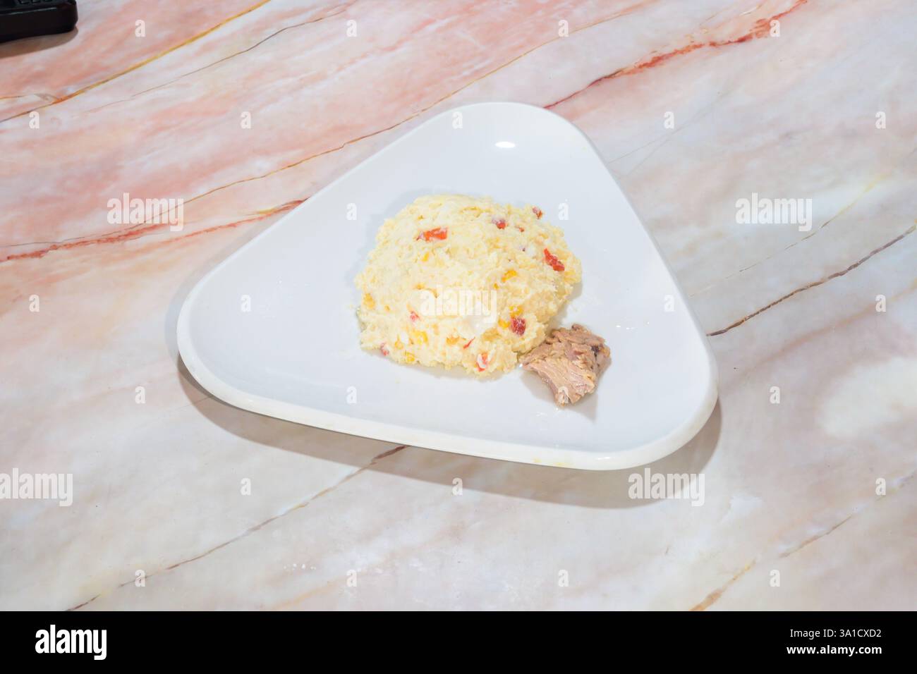 Ein dreieckiger Teller Essen mit einem Stück Fleisch drauf. Der Teller ist weiß und das Fleisch braun Stockfoto
