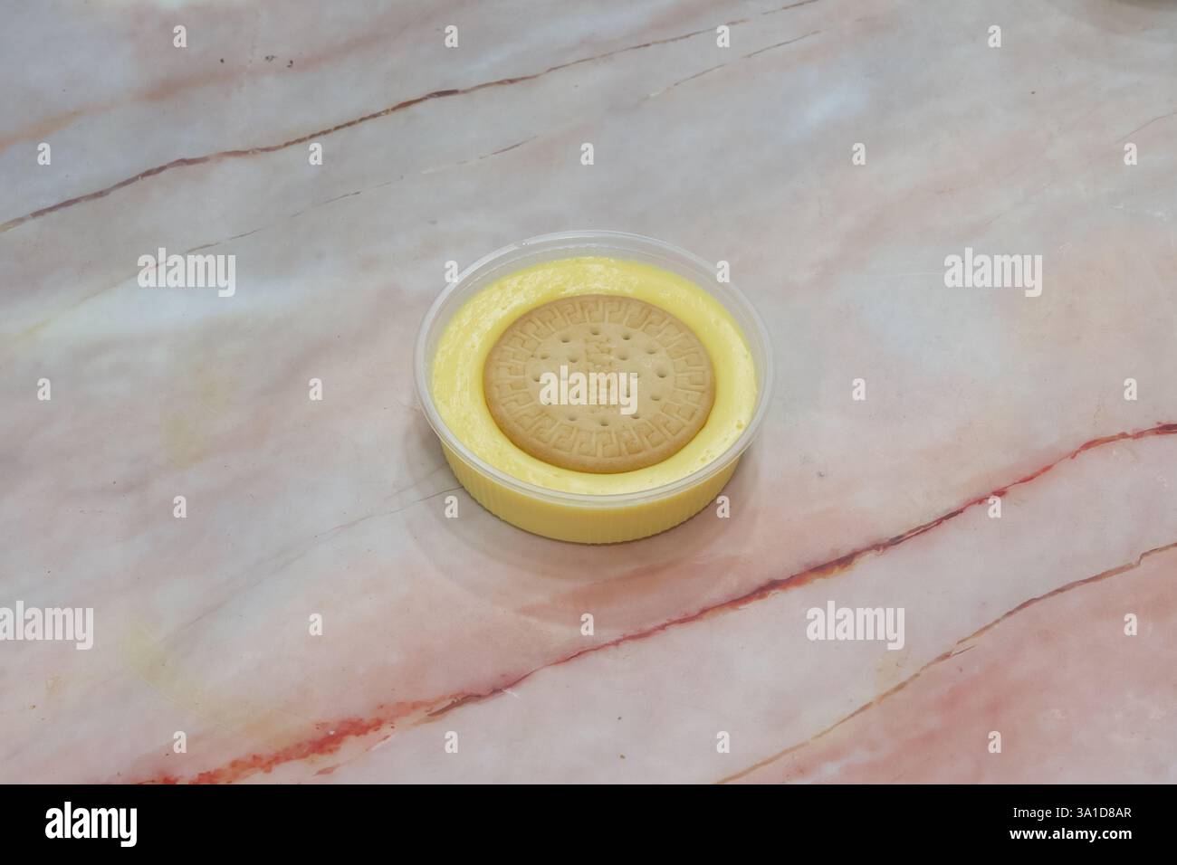 Ein kleiner Behälter mit gelber Creme und einem Keks drauf. Das Konzept von Genuss und Komfort als Kombination aus cremigem Dessert und knusprigem Co Stockfoto