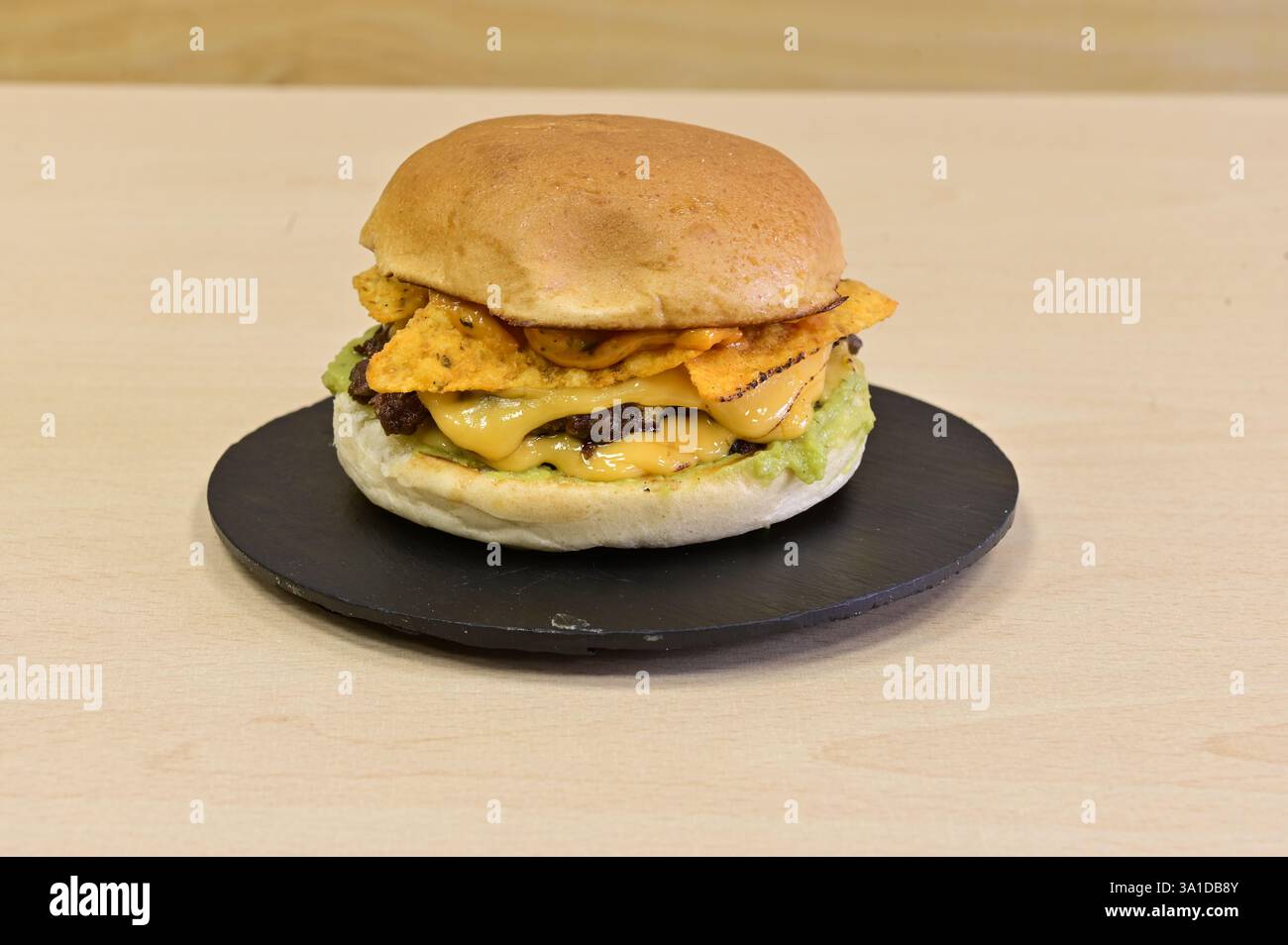 Ein großer Hamburger mit Käse und Bohnen auf einem schwarzen Teller ... Ein großer Hamburger mit Käse und Bohnen auf einem schwarzen Teller ...