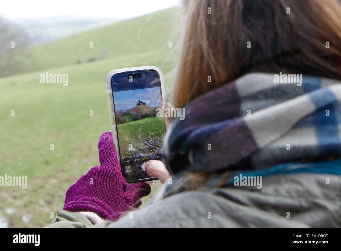 Frau, die Landschaftsfotos mit Smartphone auf dem Land macht, trägt Handschuhe und Schal bei kaltem Wetter. Colmers Hill, Symondsbury Anwesen westlich von dorset, großbritannien Stockfoto