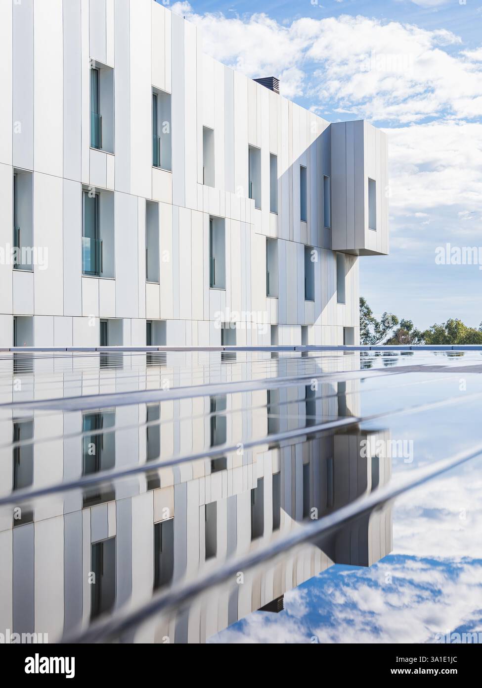 Die schlanken Linien eines modernen Gebäudes in Barcelona spiegeln sich in einer ruhigen Wasseroberfläche wider, die den innovativen architektonischen Stil der Stadt widerspiegelt Stockfoto