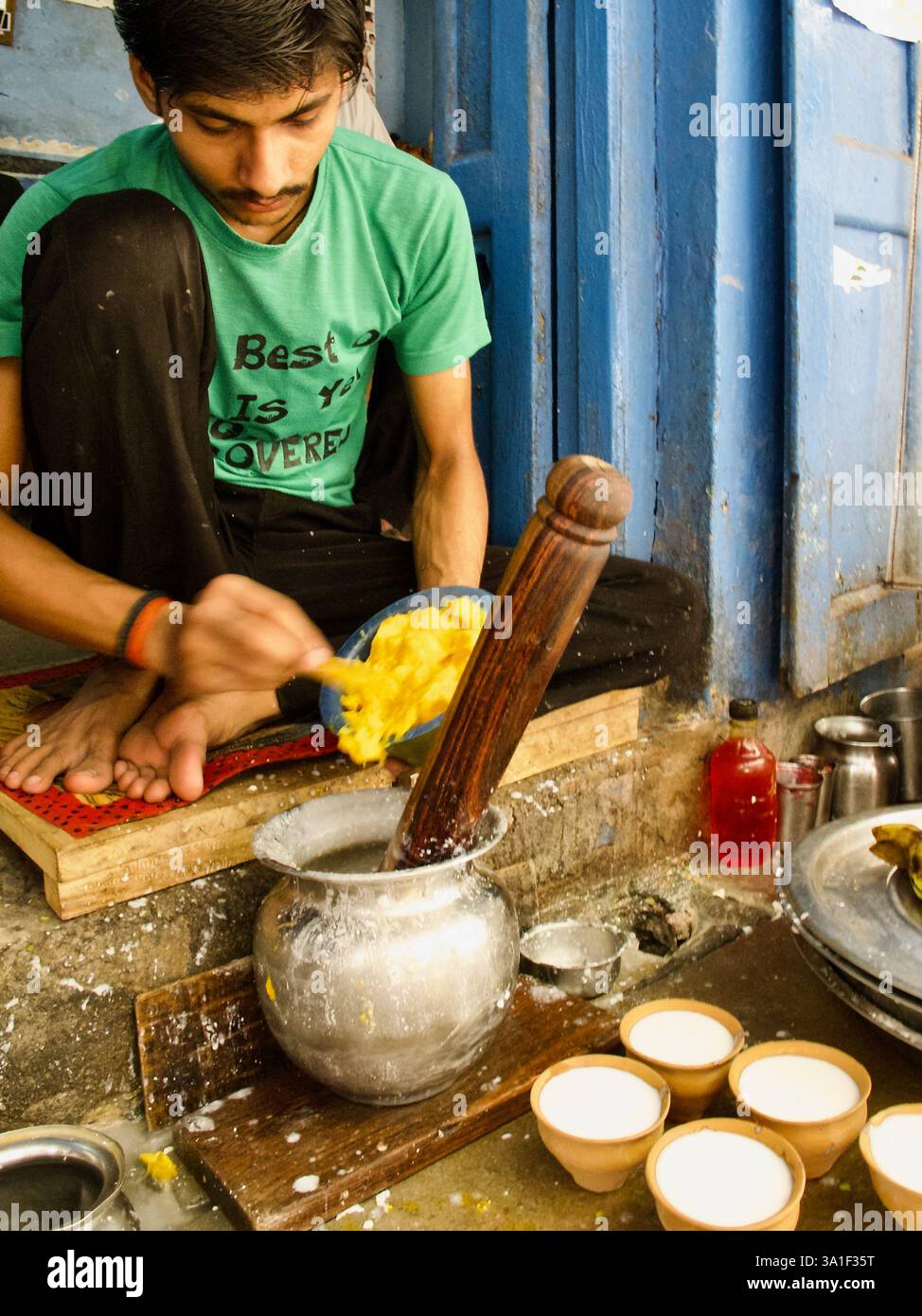 Junger Mann bereitet frische Mango-Lassi am beliebten Straßenstand Blue Lassi in Varanasi zu, serviert in traditionellen Tonbechern für Einheimische und Touristen. Stockfoto