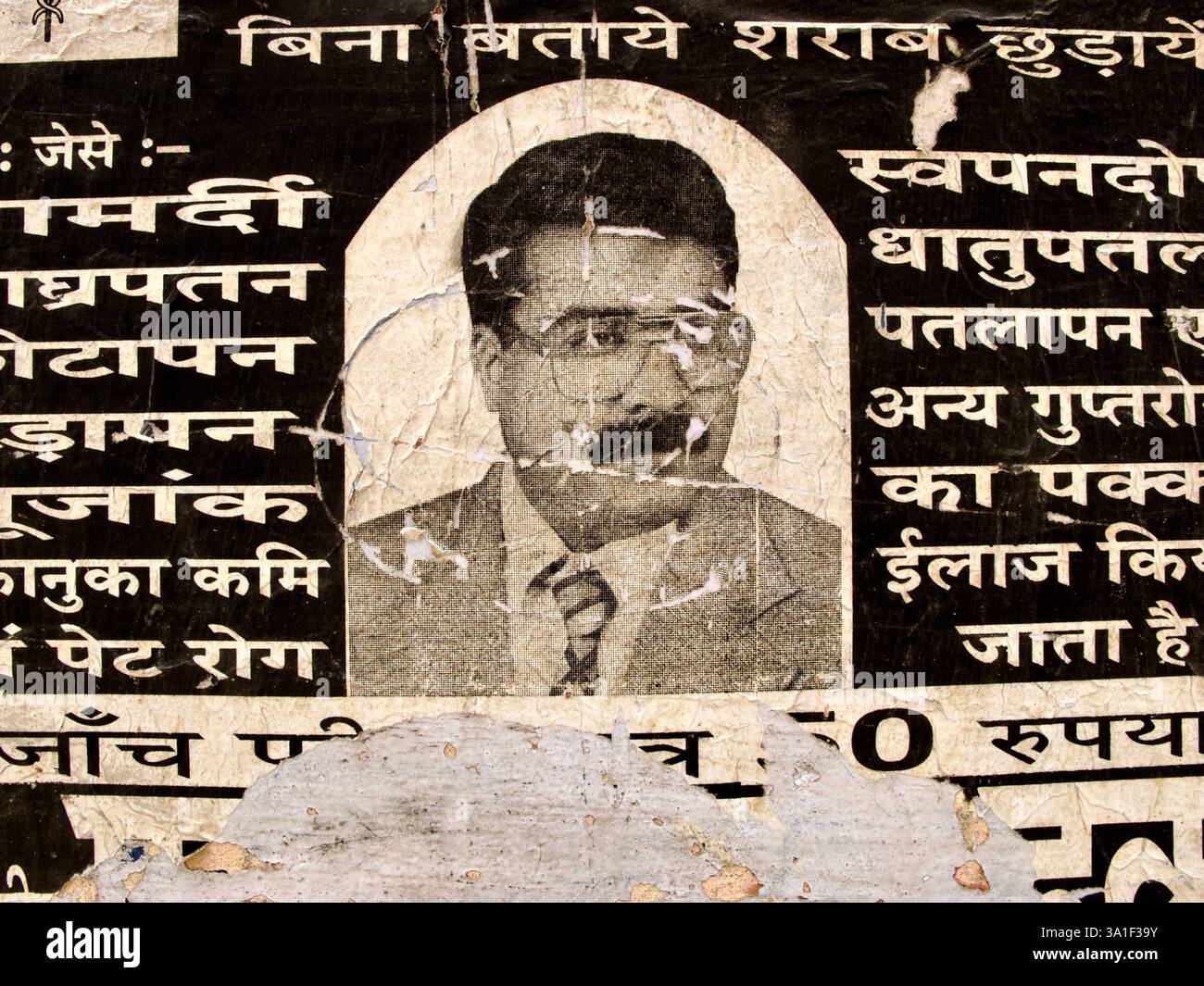 Verwitterte hindi-sprachige Werbung mit einem Arzt-Porträt, das Behandlungen für sucht und gesundheitliche Probleme anbietet, an einer Straßenwand angebracht. Stockfoto