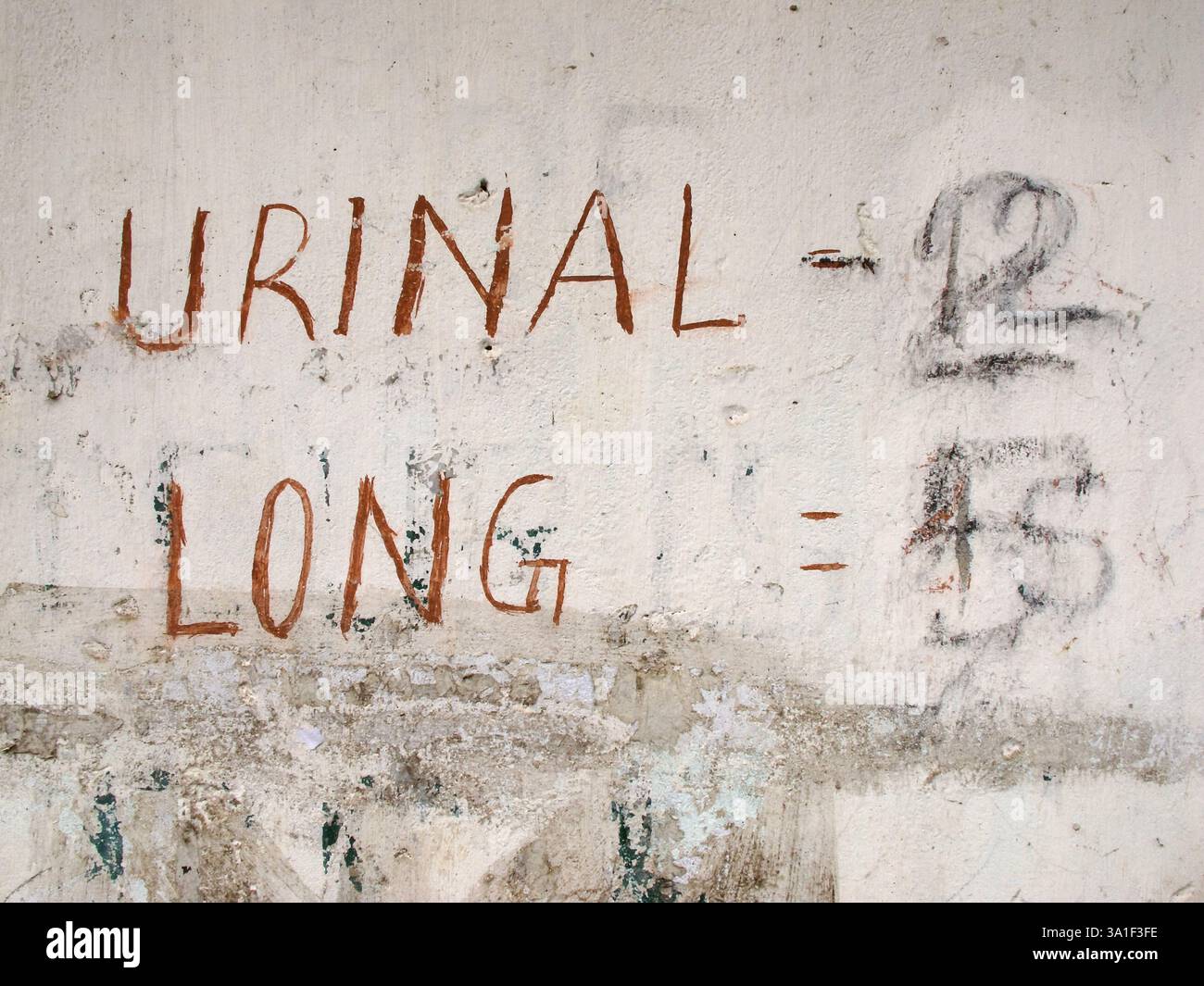 Handgemalte Preisliste für ein öffentliches Urinal an einer verwitterten Wand an einer Bushaltestelle in Indien, die informelle Infrastruktur widerspiegelt. Stockfoto