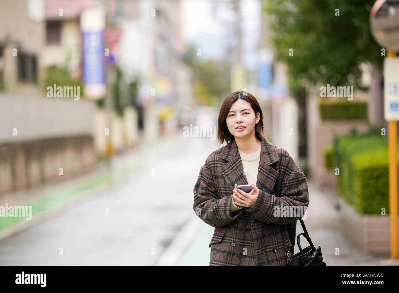 Eine 29-jährige Japanerin in einem karierten Mantel. Sie läuft durch Gassen mit wenigen japanischen Autos in der Hand. Stockfoto