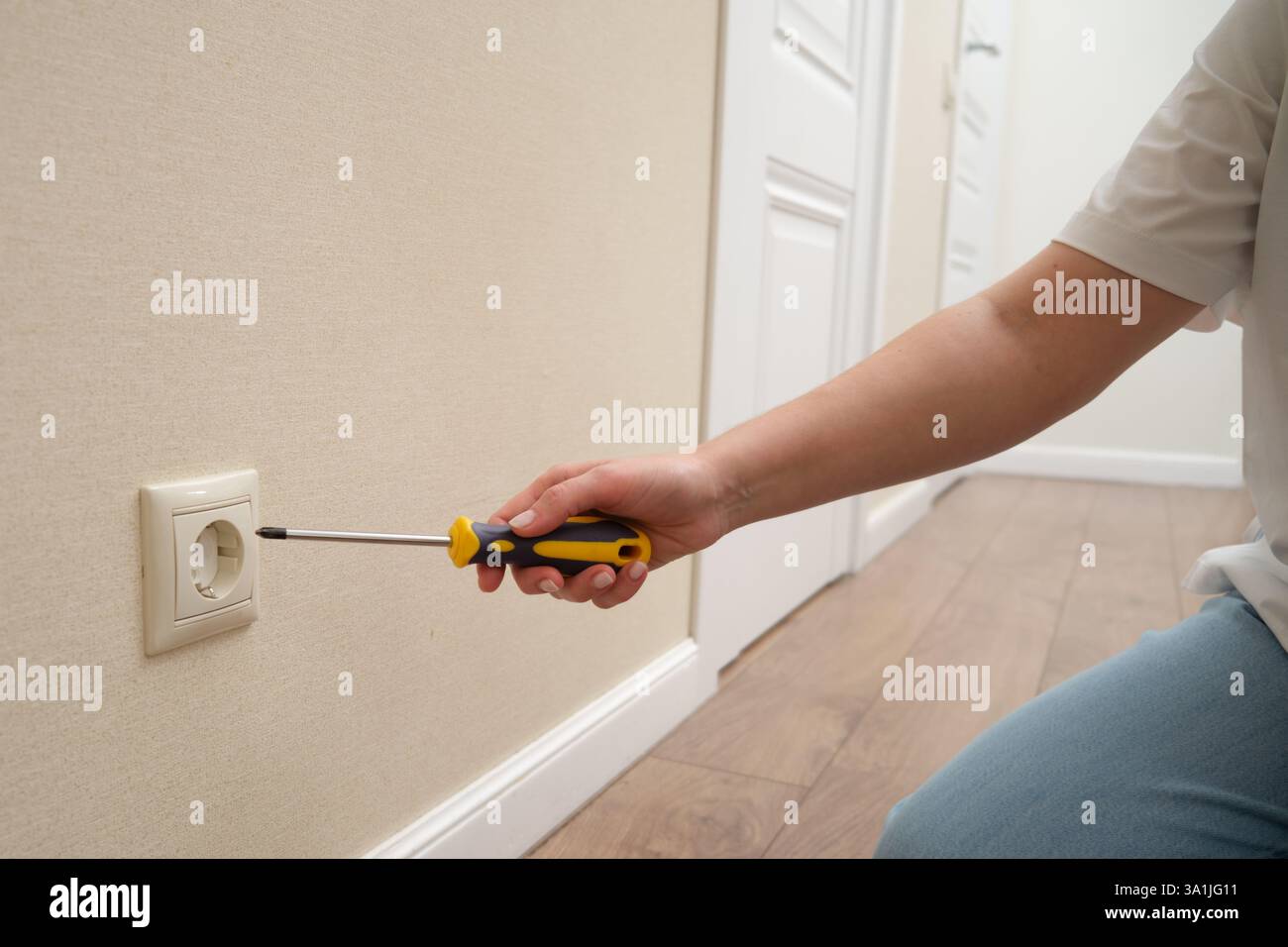 Person, die die Steckdose mit einem Schraubendreher an der beigefarbenen Wand repariert. Hauswartung und elektrisches Arbeitskonzept Stockfoto