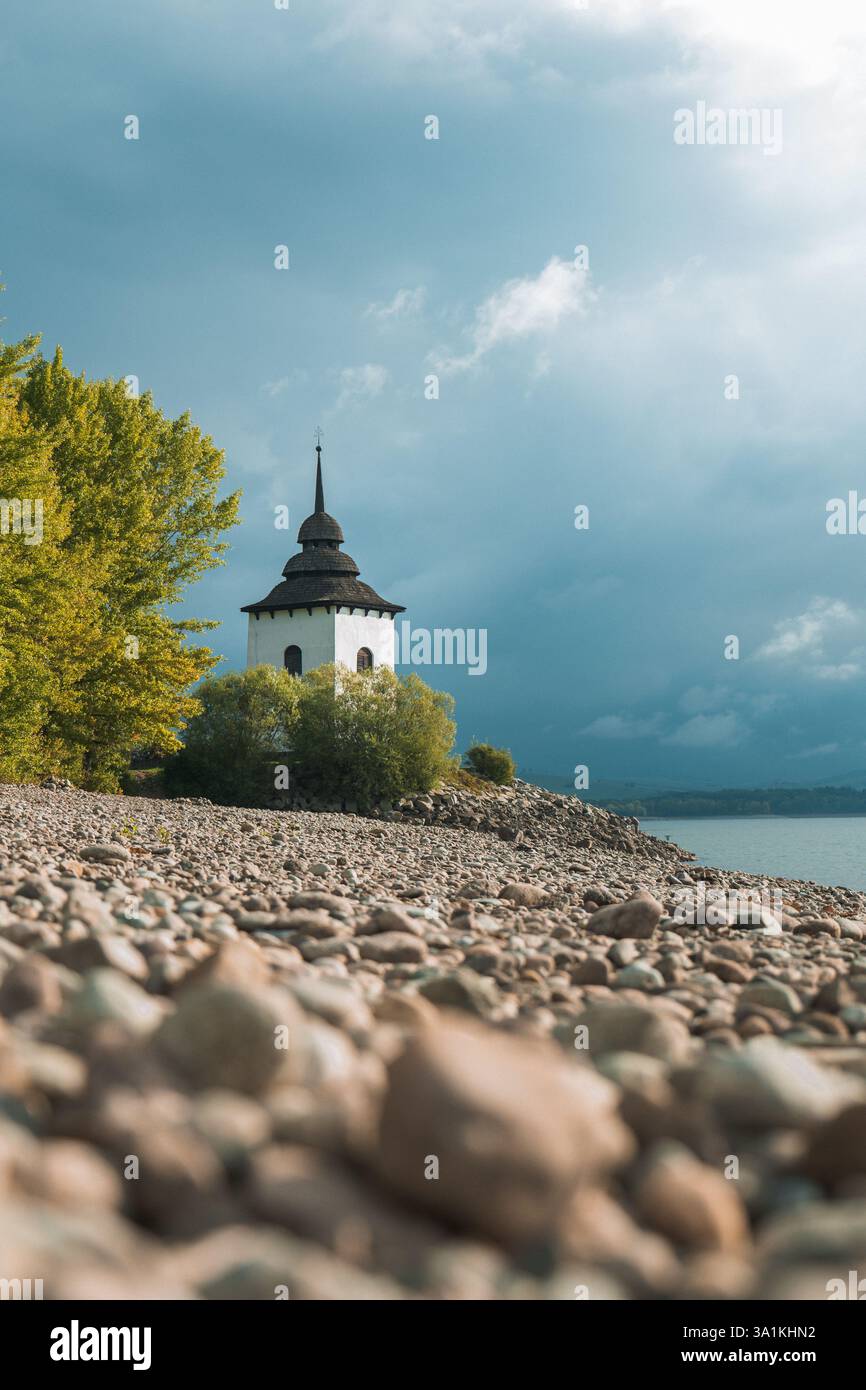 Alte Kirche mit Wolken im Hintergrund, fotografiert von einem felsigen Ufer eines Reservoir Stockfoto
