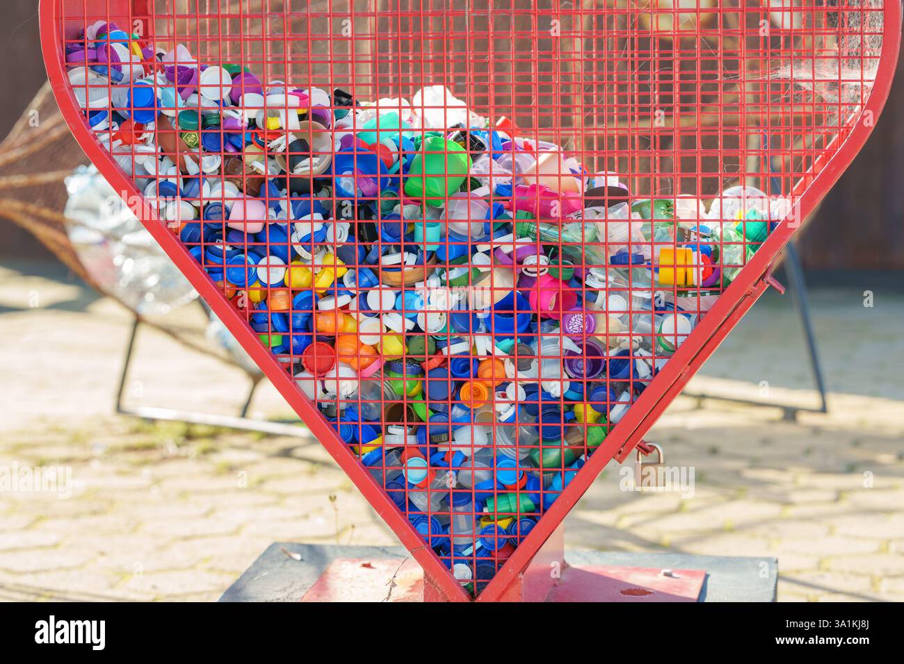 Altura, Portugal, 19. Februar 2025. Recyclingbehälter in Form eines Herzens, gefüllt mit Plastikverschlüssen in verschiedenen Farben. Stockfoto