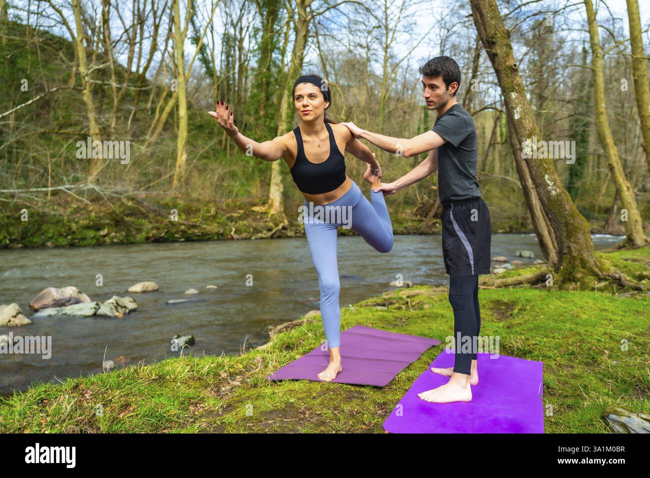 Yogalehrer üben Uthita Hasta padangustasana Pose an einem ruhigen Fluss, umgeben von üppiger Natur und sonnen sich im Sonnenlicht Stockfoto