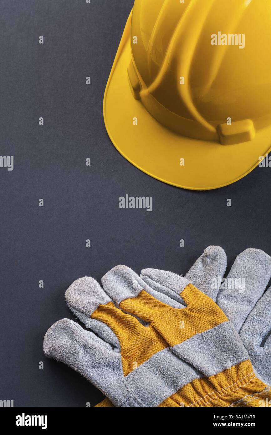 Arbeitsschutzhandschuhe und gelber Helm auf schwarzem Hintergrund Stockfoto