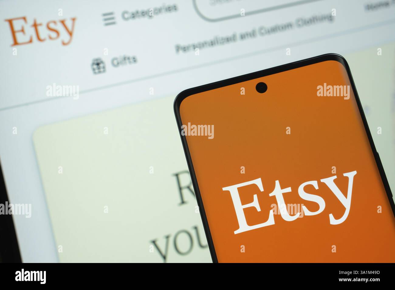 Dhaka, Bangladesch, 08. März 2025: Das Etsy-Logo wird auf einem Smartphone-Bildschirm angezeigt, wobei die Etsy-Website auf einem Computerbildschirm im Hintergrund zu sehen ist Stockfoto