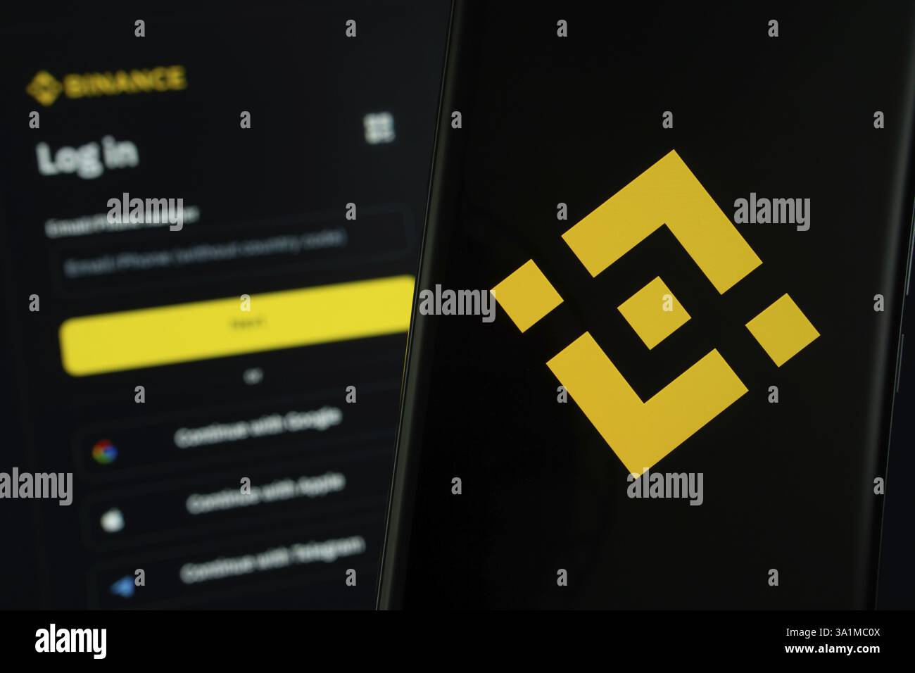 Das Binance-Logo wird auf einem Smartphone-Bildschirm angezeigt, wobei die binance-Anmeldeseite auf einem Computerbildschirm im Hintergrund sichtbar ist Stockfoto