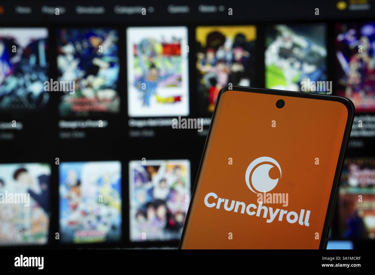 Das Crunchyroll-Logo wird auf einem Smartphone-Bildschirm angezeigt, wobei die Crunchyroll-Website auf einem Computerbildschirm im Hintergrund sichtbar ist Stockfoto