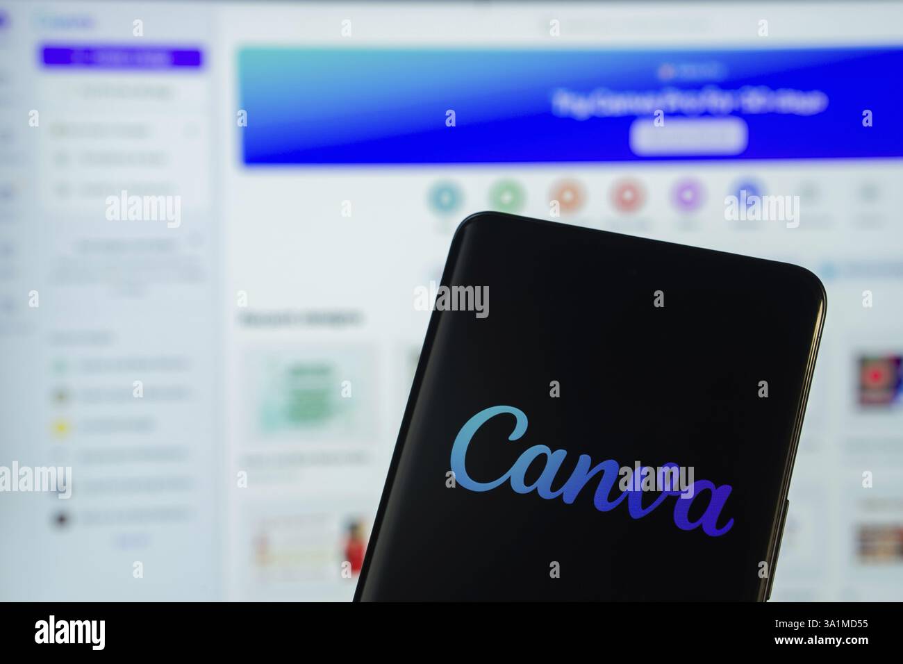Das Canva-Logo wird auf einem Smartphone-Bildschirm angezeigt, wobei die canva-Website im Hintergrund auf einem Computerbildschirm angezeigt wird Stockfoto