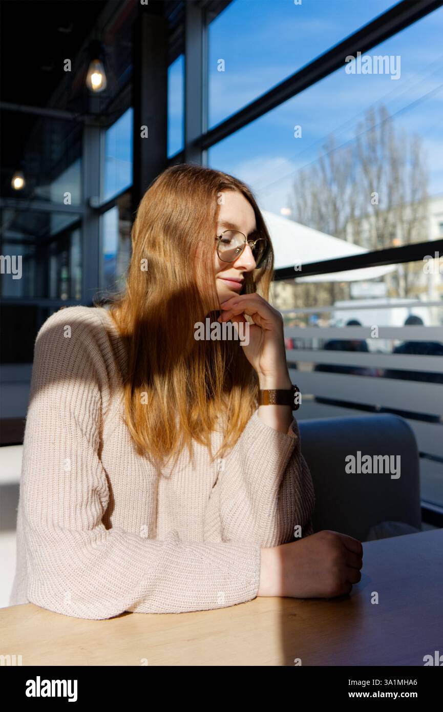 Eine Person sitzt an einem sonnigen Tisch in einem gemütlichen Café, ihr Gesicht ist teilweise verdeckt. Das warme Ambiente vermittelt eine entspannte Atmosphäre. Stockfoto