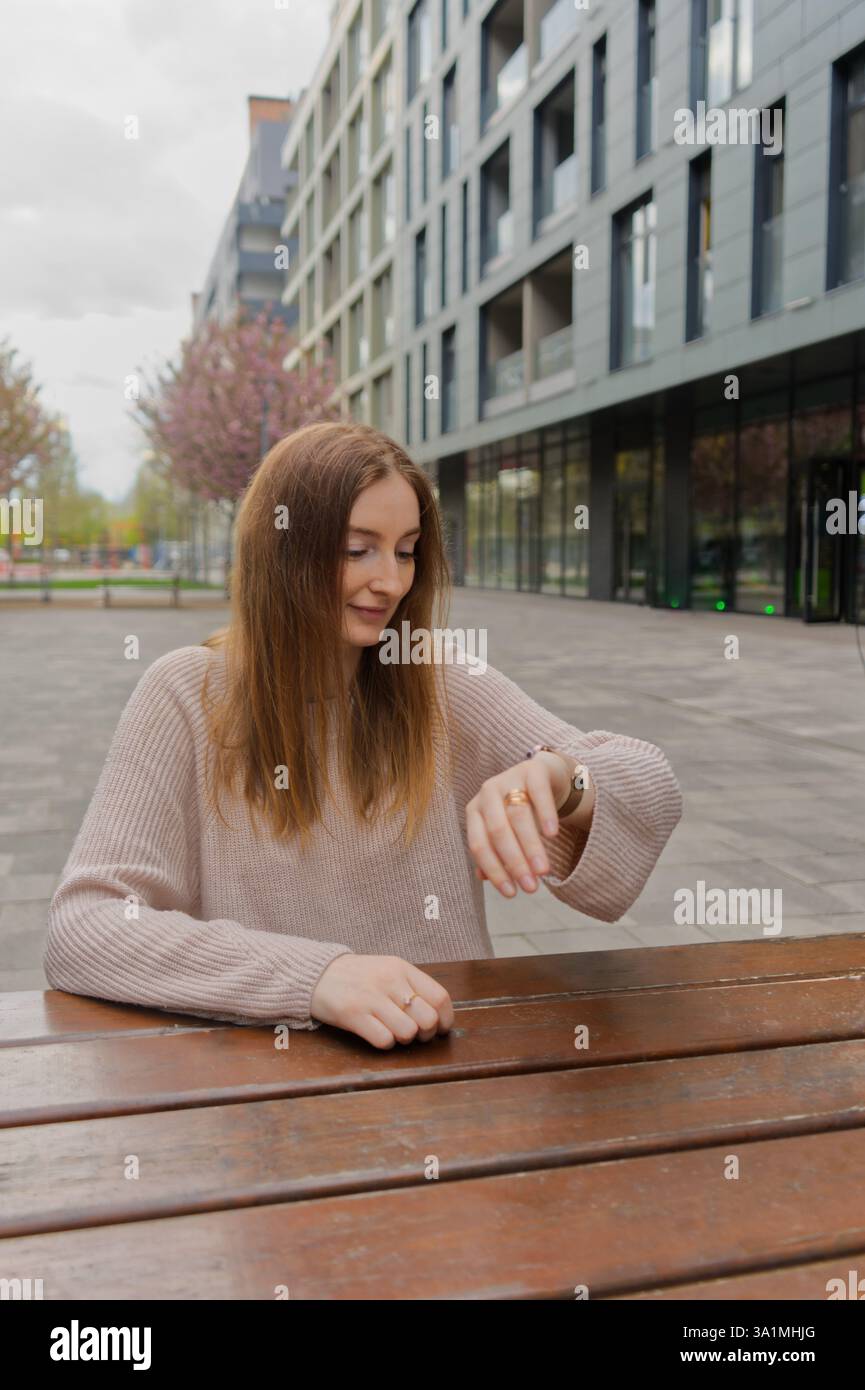 Ein Mädchen sitzt auf einer Bank und schaut sich die Zeit an Stockfoto