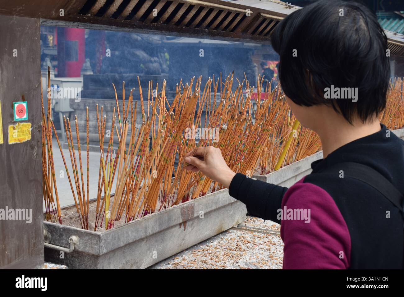 Ein heiterer Moment, in dem eine Frau in einem Tempel in Hongkong Weihrauch verbrennt, symbolisiert spirituelle Verbindung und kulturelle Traditionen in einer heiligen Umgebung. Stockfoto
