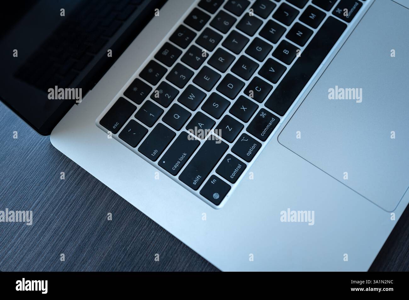 Nahaufnahme einer MacBook-Tastatur und eines Trackpads auf einem dunklen Holzpult mit schwarzen Tasten, Aluminiumgehäuse und partieller Bildschirmreflexion Stockfoto