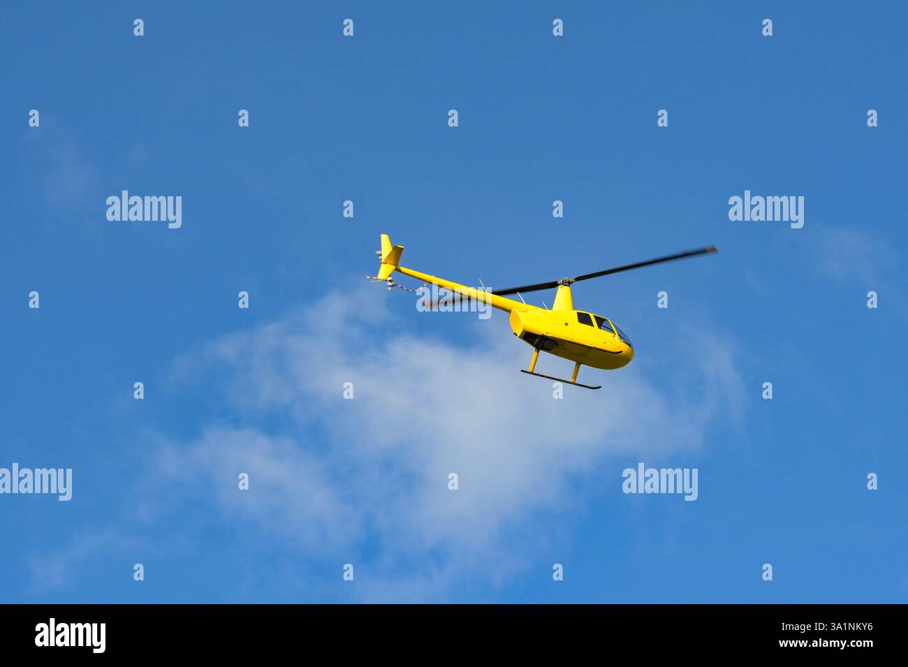 Gelber Hubschrauber im Flug gegen einen blauen Himmel Stockfoto