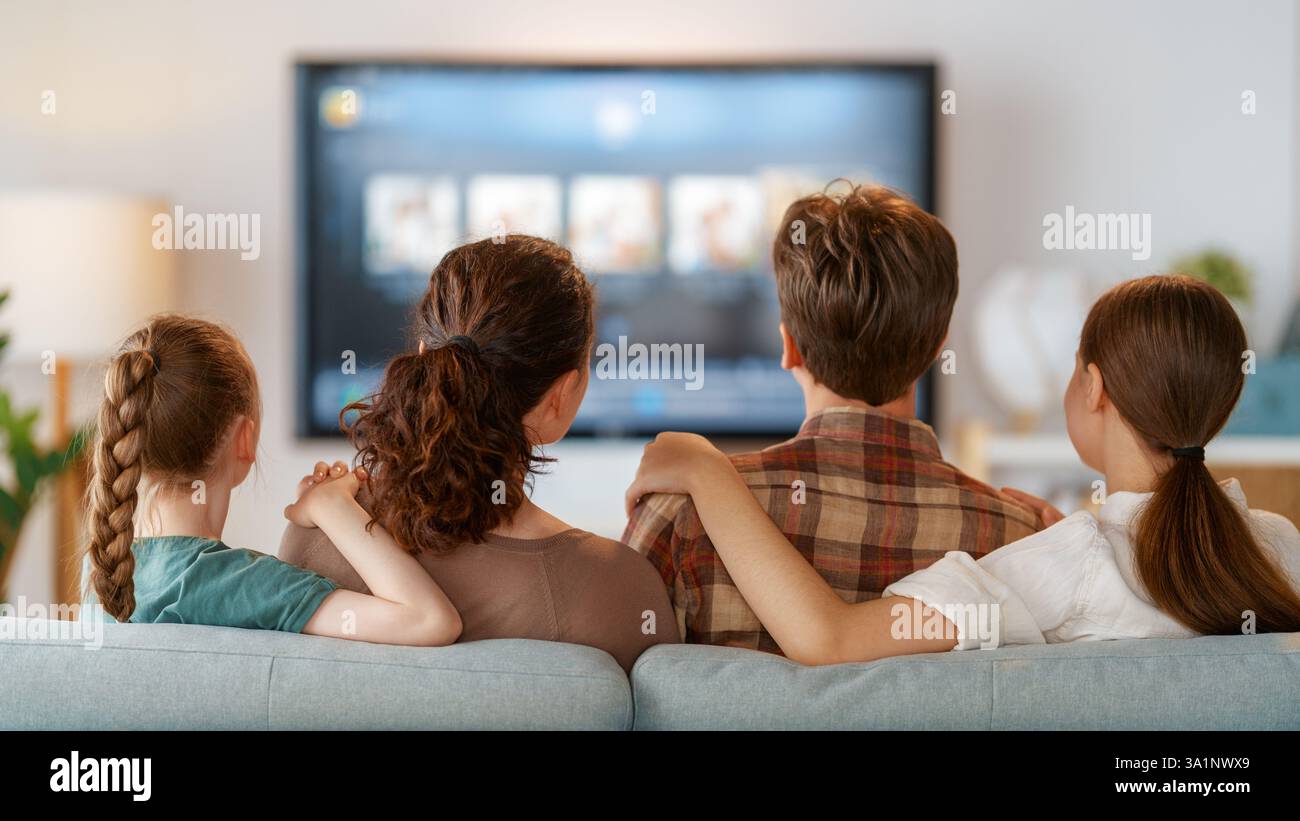 Glückliche Familie, die Zeit miteinander verbringt. Mutter, Vater und Kinder schauen fern, Filme mit Popcorn am Abend zu Hause. Stockfoto