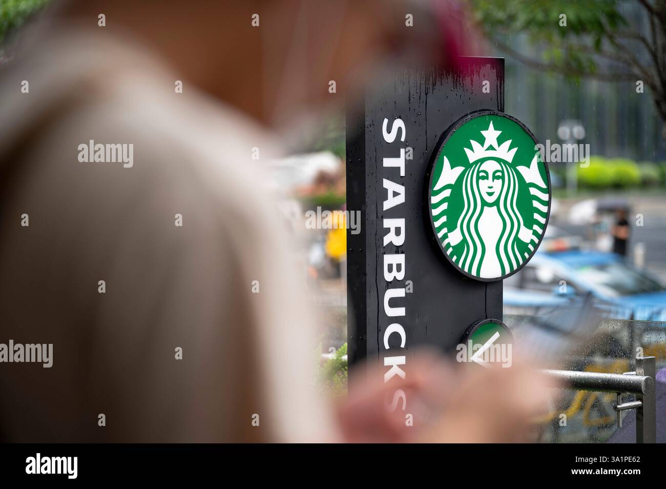 Ein Mann benutzt sein Handy als das amerikanische Starbucks Coffee Logo und Geschäft im Hinterhof in Shenzhen, China. Stockfoto