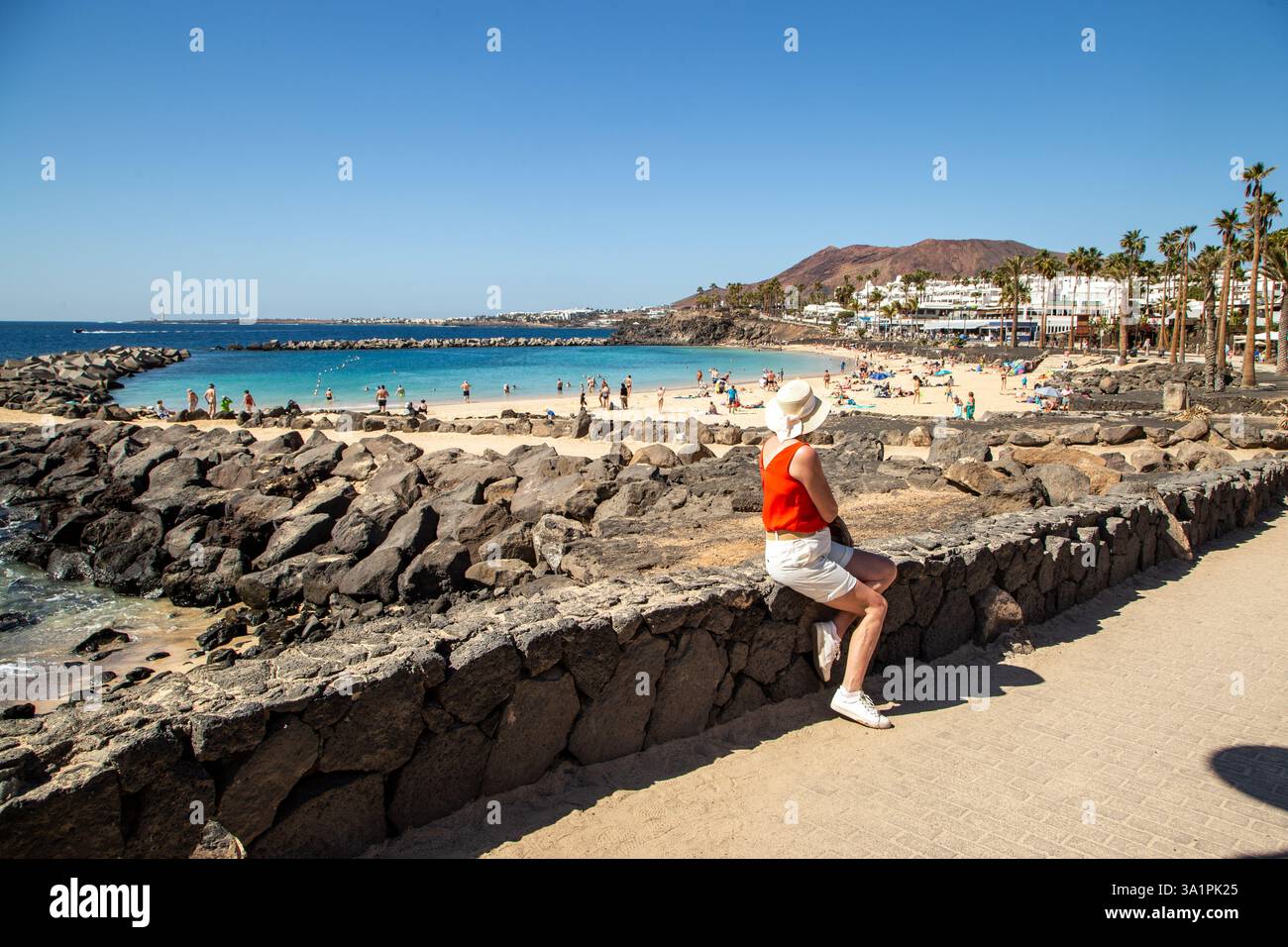 Touristen und Urlauber am Strand von Playa Blanca auf den spanischen Kanarischen Inseln auf Lanzarote mit dem Roten Bergvulkan Montana Roja dahinter Stockfoto