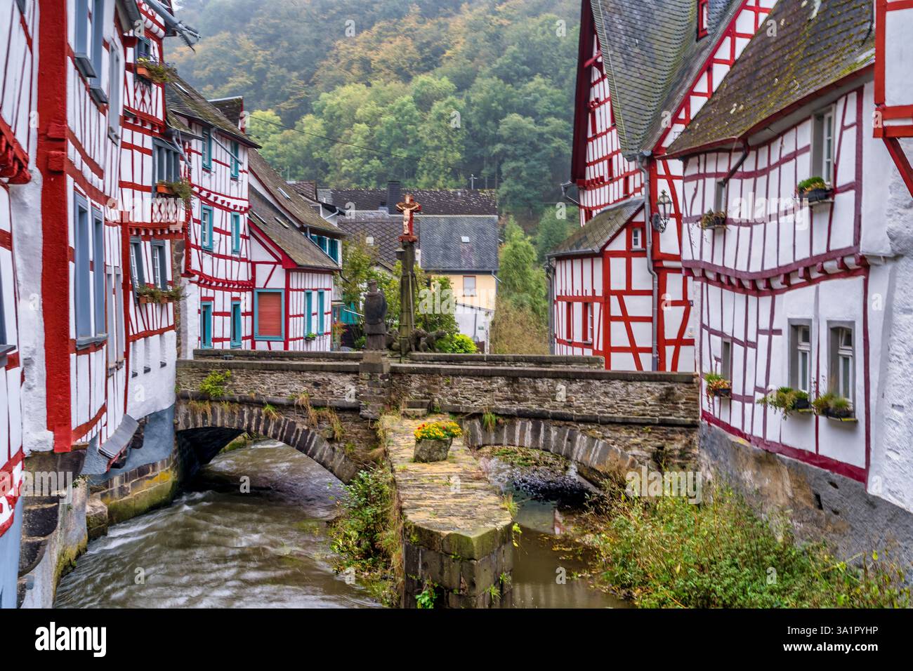 Mittelalterliche rote Fachwerkhäuser im Monreal Deutschland mit Brücke über dem Elzbach mit Kruzifix Stockfoto