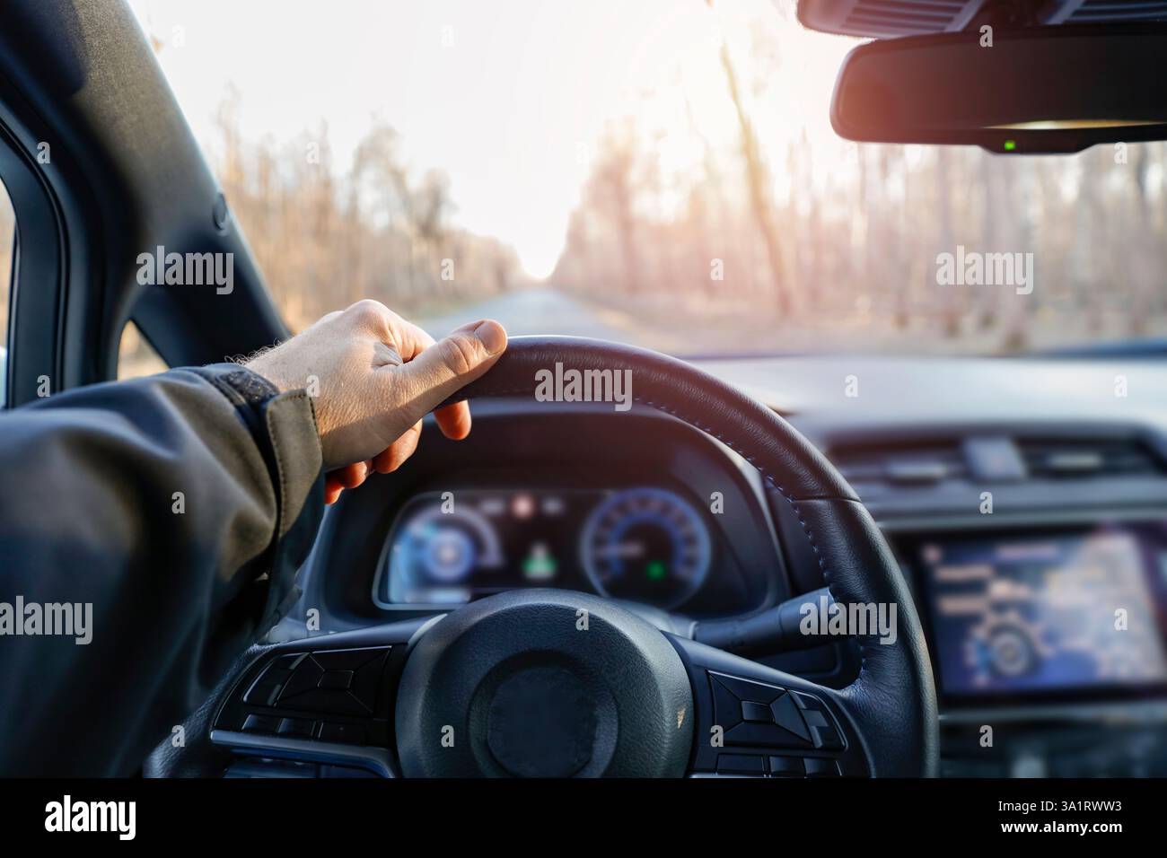 Autofahrer, der auf der Autobahn fährt. Die Hand einer Person am Lenkrad eines Autos, die auf einer bewaldeten Straße fährt. Innenraum des Fahrzeugs mit Armaturenbrett. Stockfoto