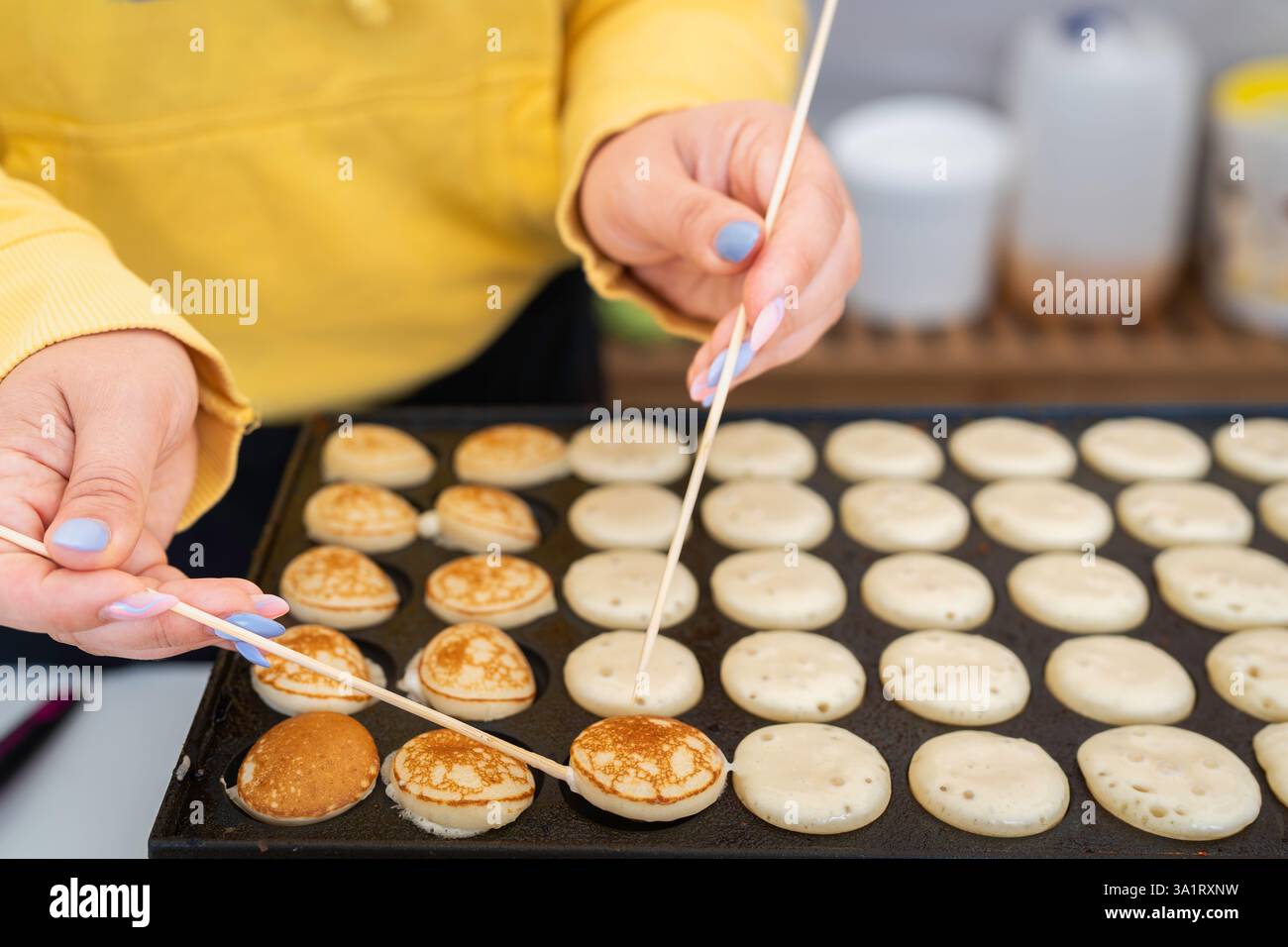 Mini-Pfannkuchen auf der Pfannkuchenmaschine machen. Dutch Poffertjes – winzige Pfannkuchen, die auf einer Eisenpfanne gebacken werden und während des Street Food Festivals zubereitet werden. Stockfoto