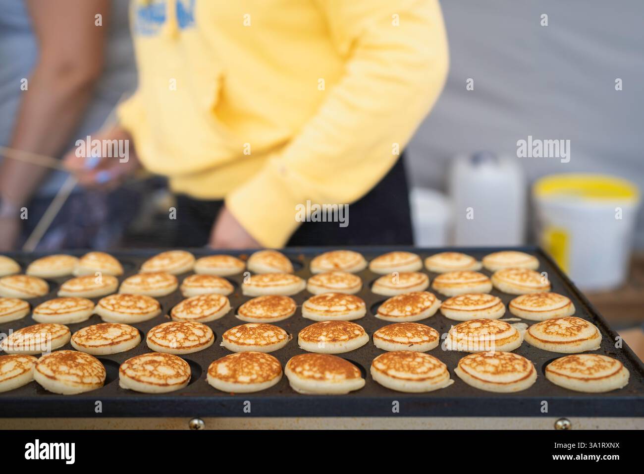 Mini-Pfannkuchen auf der Pfannkuchenmaschine machen. Dutch Poffertjes – winzige Pfannkuchen, die auf einer Eisenpfanne gebacken werden und während des Street Food Festivals zubereitet werden. Stockfoto