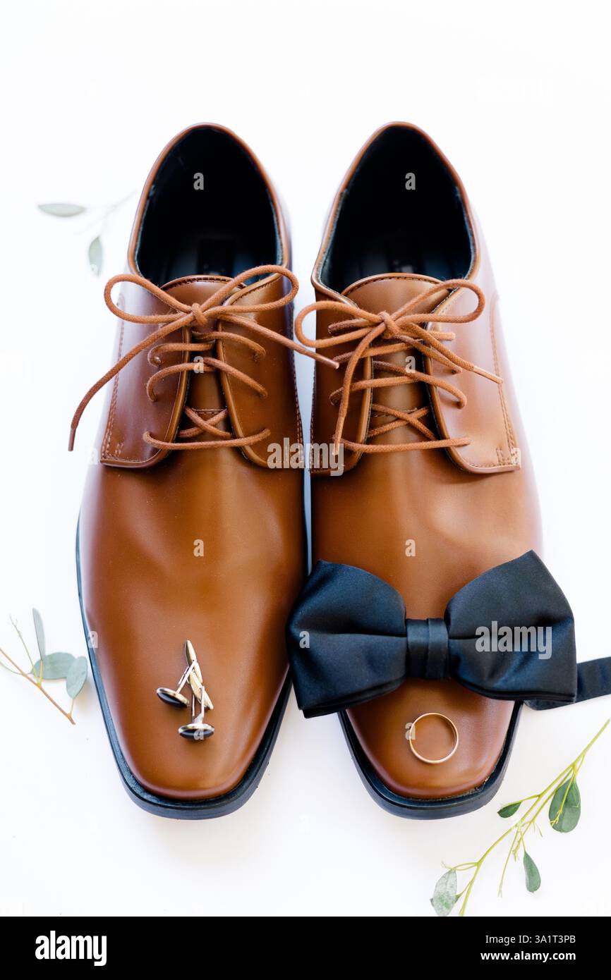 Braune Schuhe mit schwarzer Schleife, Manschettenknöpfen und Ehering. Stockfoto