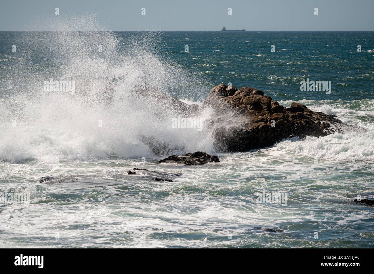 Wellen, die unter hellem Sonnenlicht auf dem offenen Meer gegen die felsige Küste krachen Stockfoto