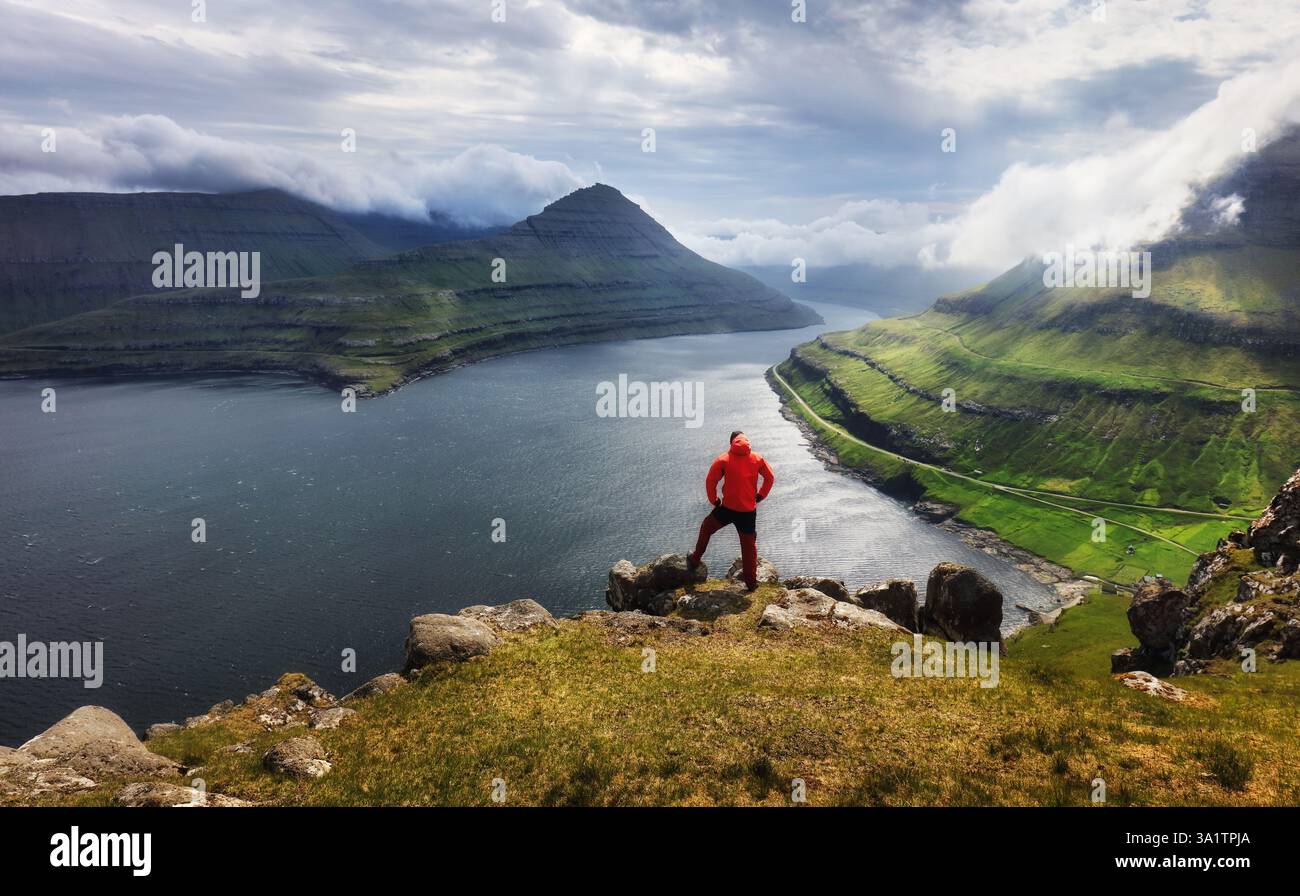 Touristen in einer roten Jacke erkunden die natürlichen Sehenswürdigkeiten. Sommerberglandschaft Blick auf den Funningur Fjord vom Gipfel Funningur. Eysturoy Island, Färöer Stockfoto