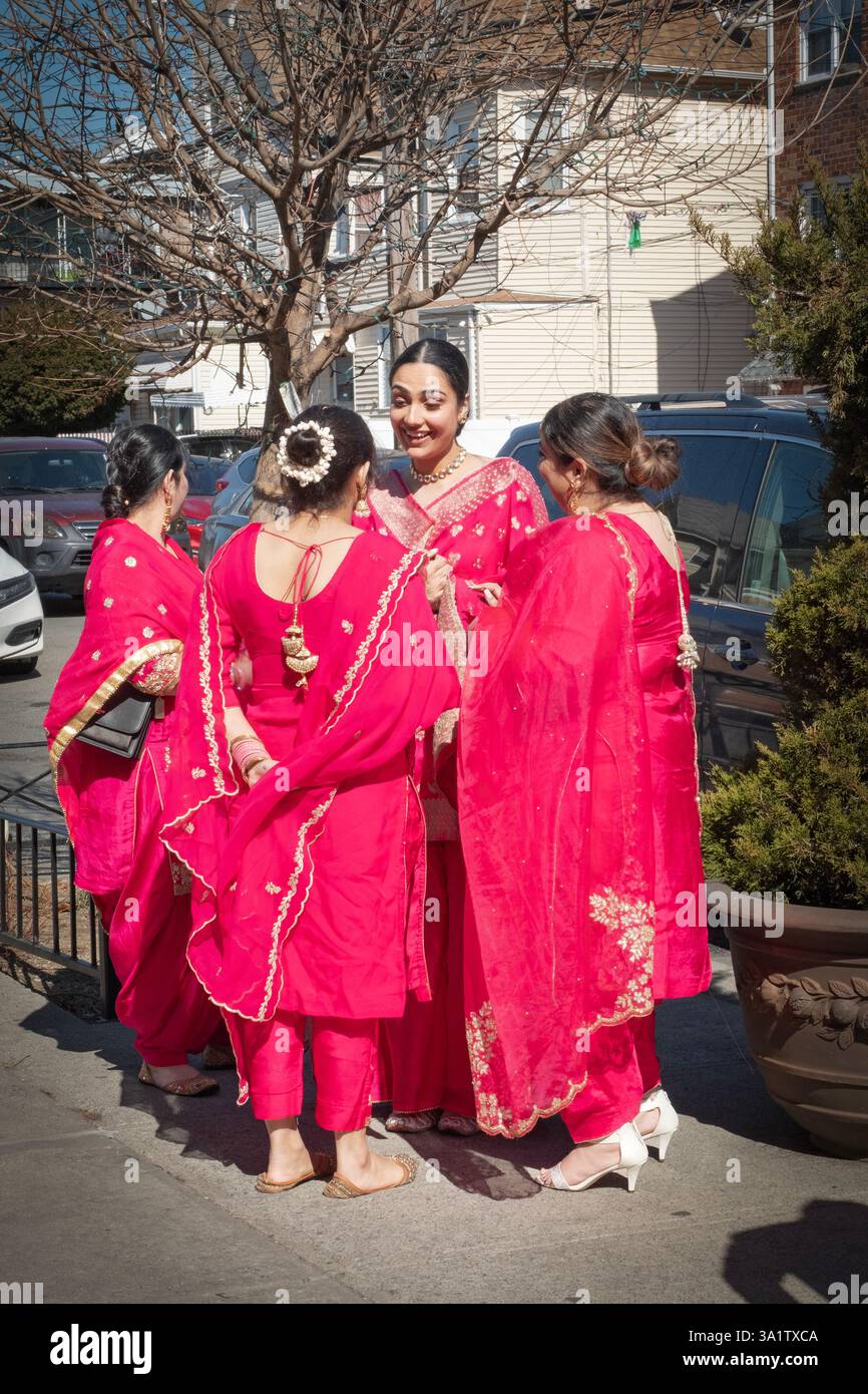 4 Frauen in roten lehenga-Kleidern unterhalten sich vor einem Tempel vor dem Beginn einer Sikh-Hochzeit. In Queens, New York, ein sehr vielfältiges Hotel. Stockfoto