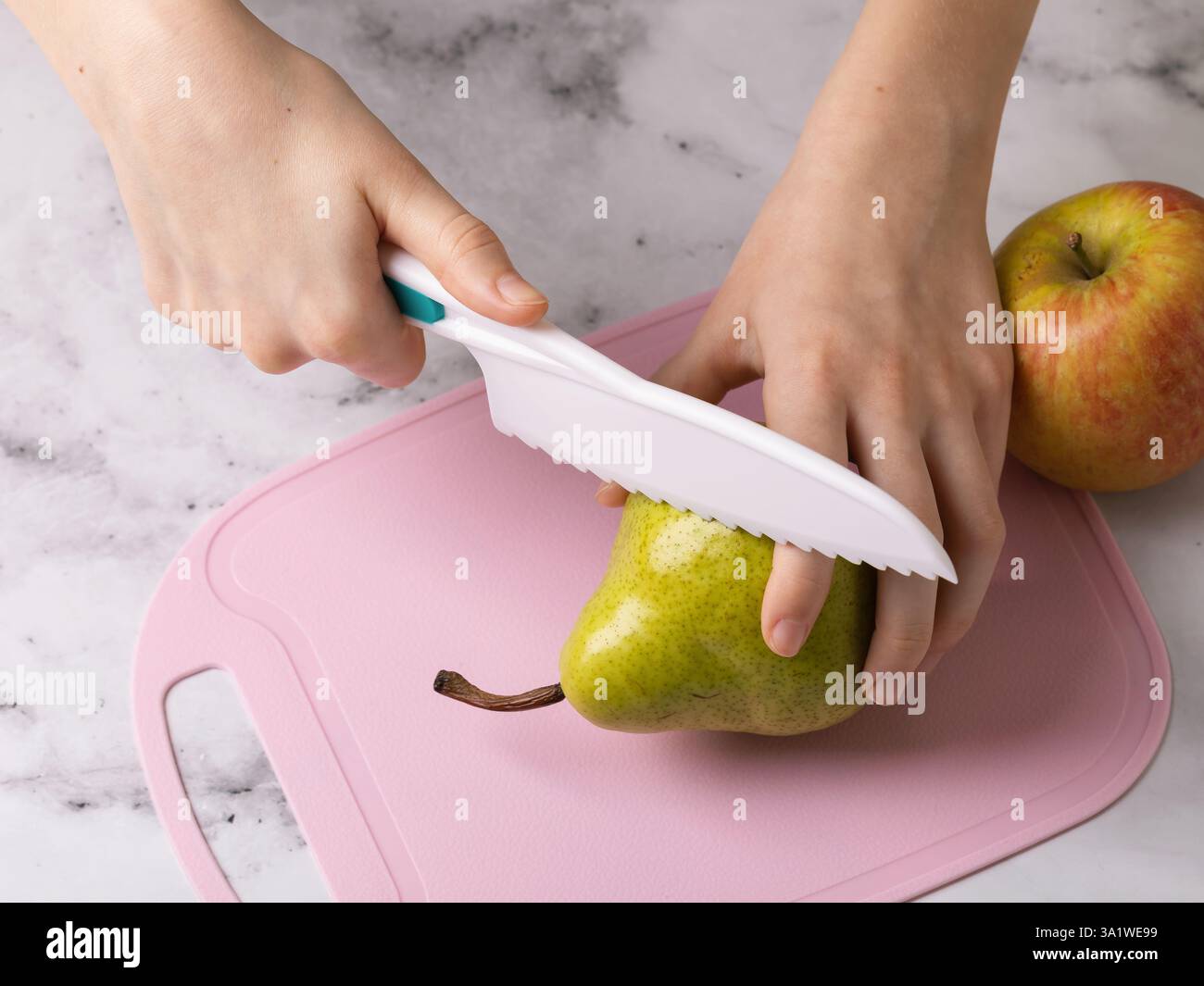Kind schneidet Birne mit Kunststoffmesser und trifft versehentlich den Zeigefinger, Konzept zur Sicherheit von Kunststoffmessern für Kinder Stockfoto