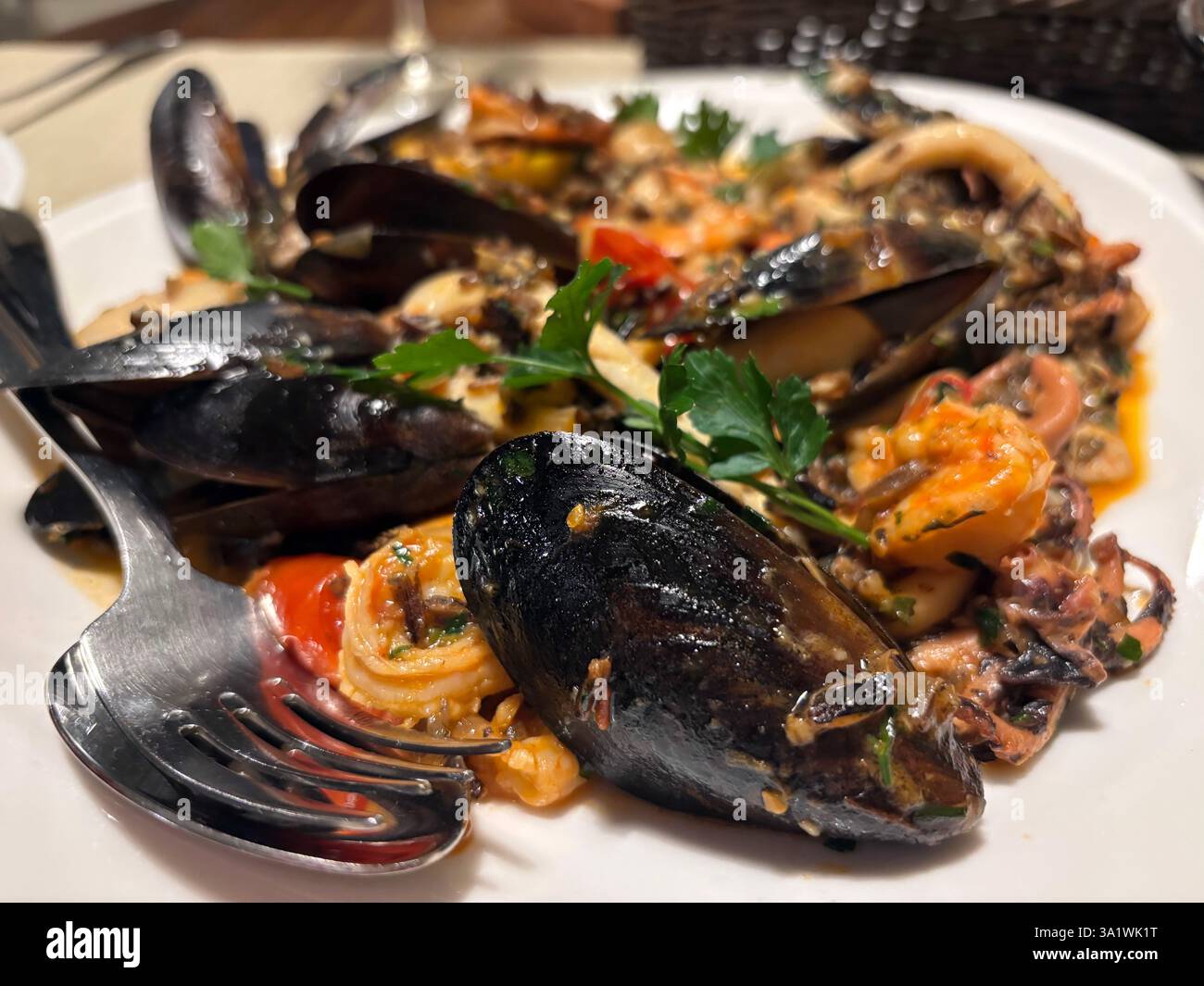 Nahaufnahme, detaillierte Ansicht, Gourmet-Gericht wilder Reis mit Meeresfrüchten - Maultiere, Garnelen, Tintenfische. Löffel und Messer - bereit zum Essen. Essen im Restaurant Stockfoto