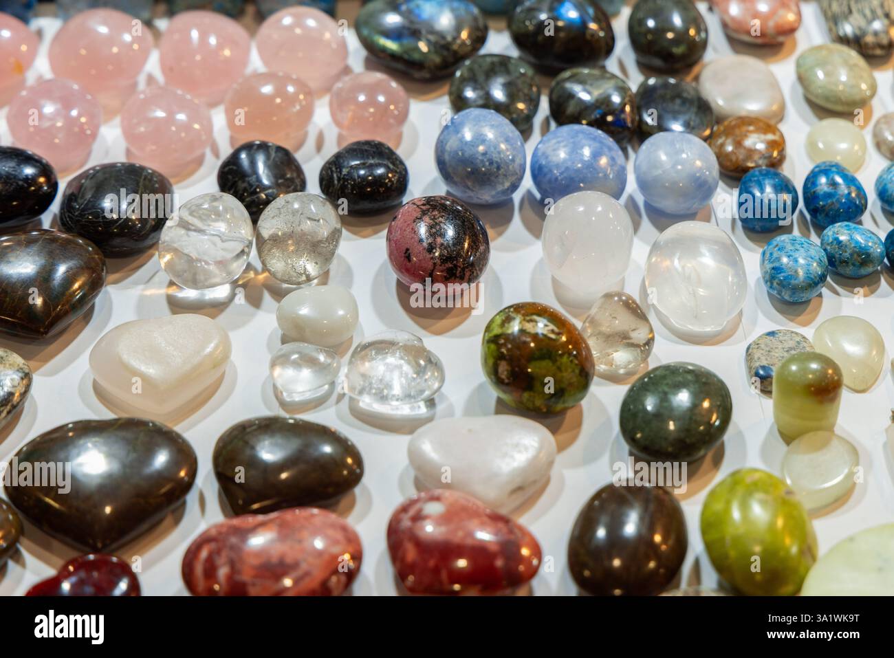 Verschiedene Trommelsteine in verschiedenen Farben und Mustern mit durchscheinenden klaren Steinen und undurchsichtigen Mineralien, die in einer dekorativen Ausstellung angeordnet sind Stockfoto